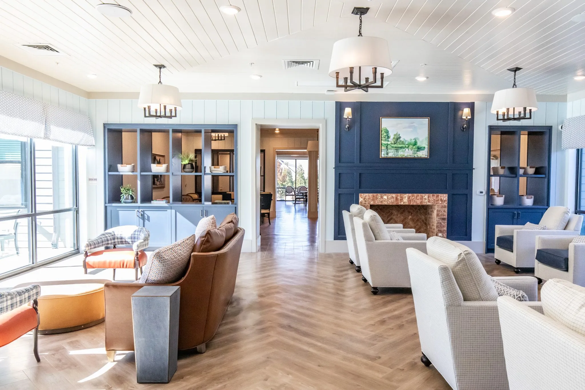 Senior living great room with navy built-in bookcases and a brick fireplace on white shiplap, cream and plaid armchairs
