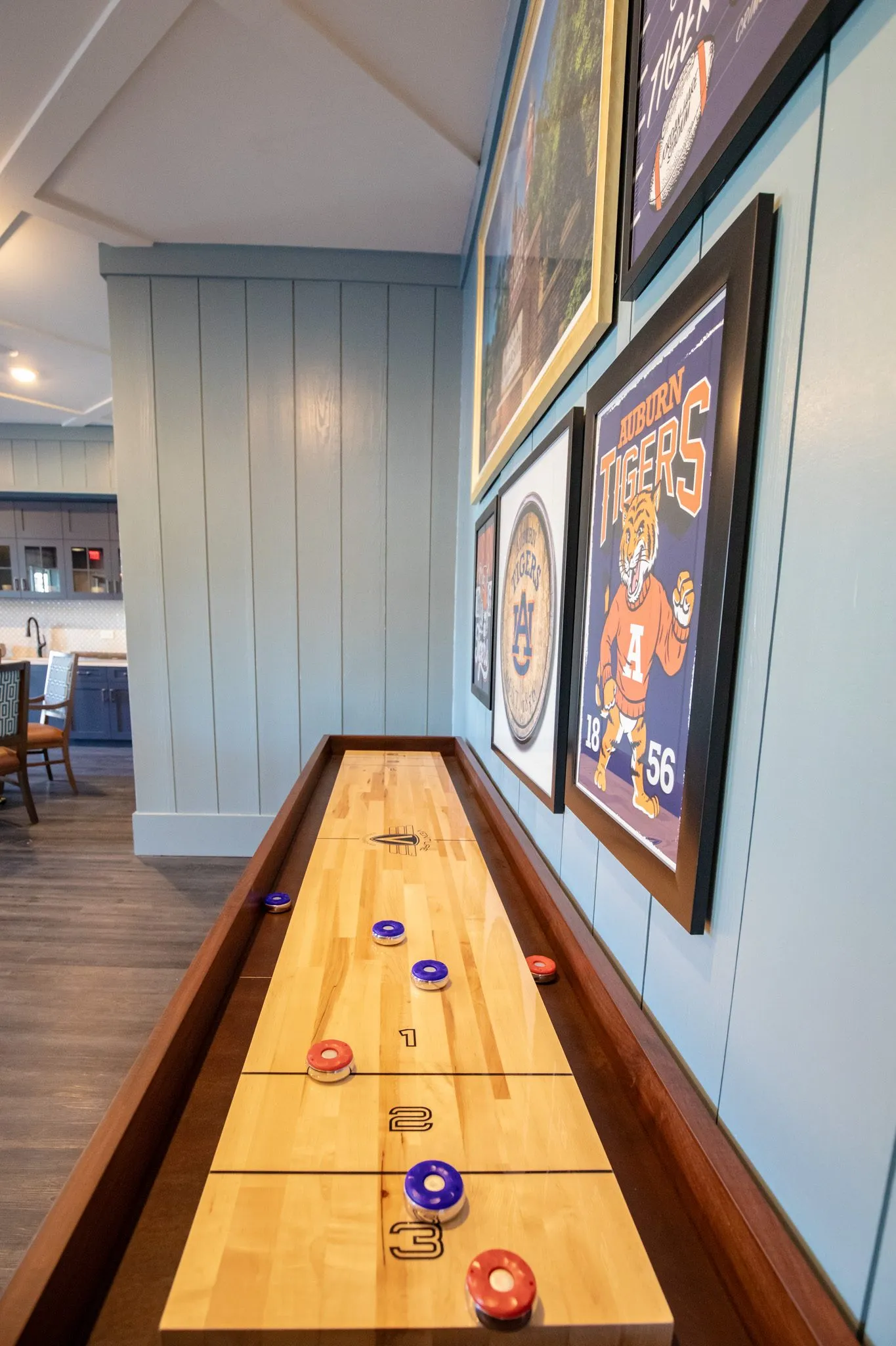 Senior living game room with a shuffleboard table running along a shiplap wall hung with collegiate posters