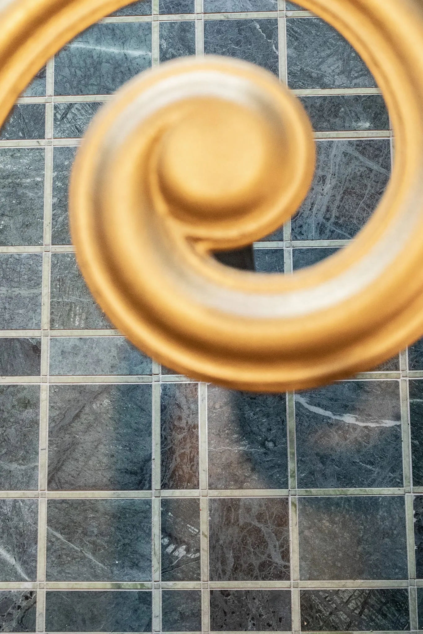 Private club interior detail: brass handrail scroll seen from above against the green marble tile floor
