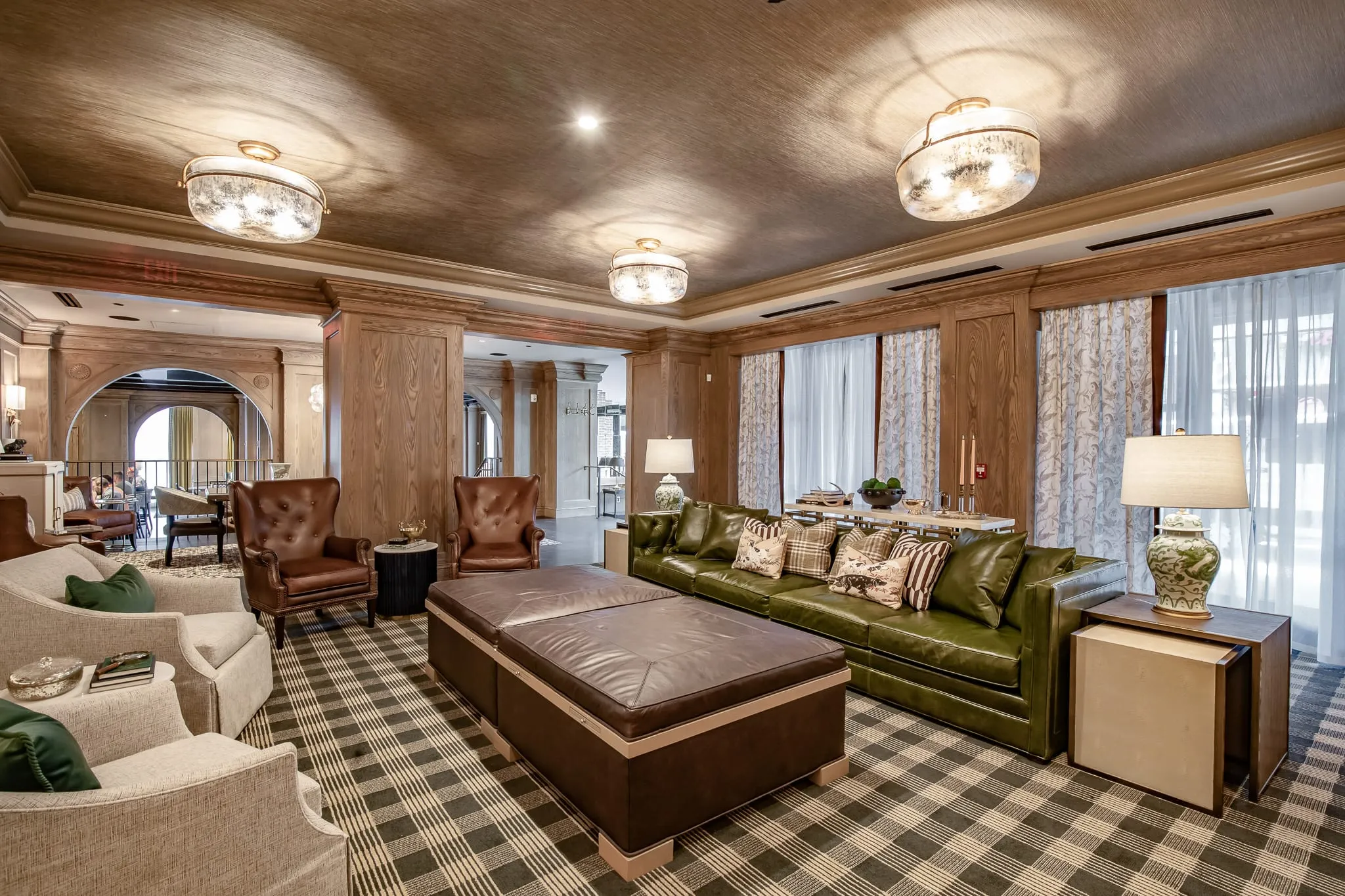 Private club lounge with an olive green leather sofa and a brown leather ottoman bench on a checked carpet