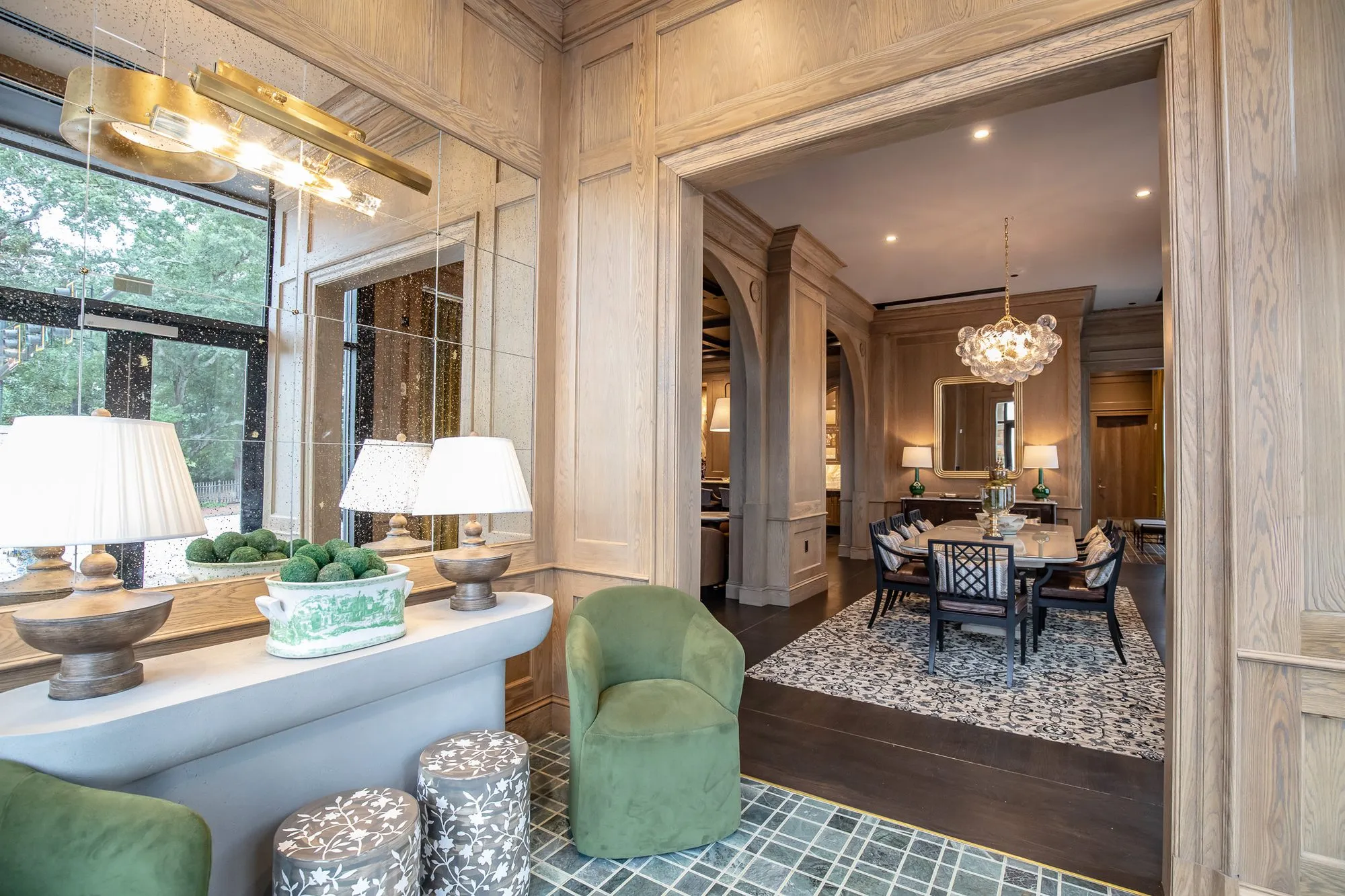 Private club foyer with green velvet chairs and a white console by the window, looking through to the dining room chandelier