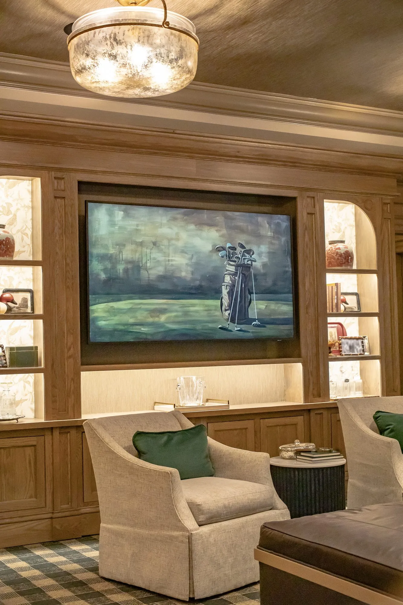 Private club interior detail: skirted armchairs before oak built-ins with lit shelves around a large golfer painting