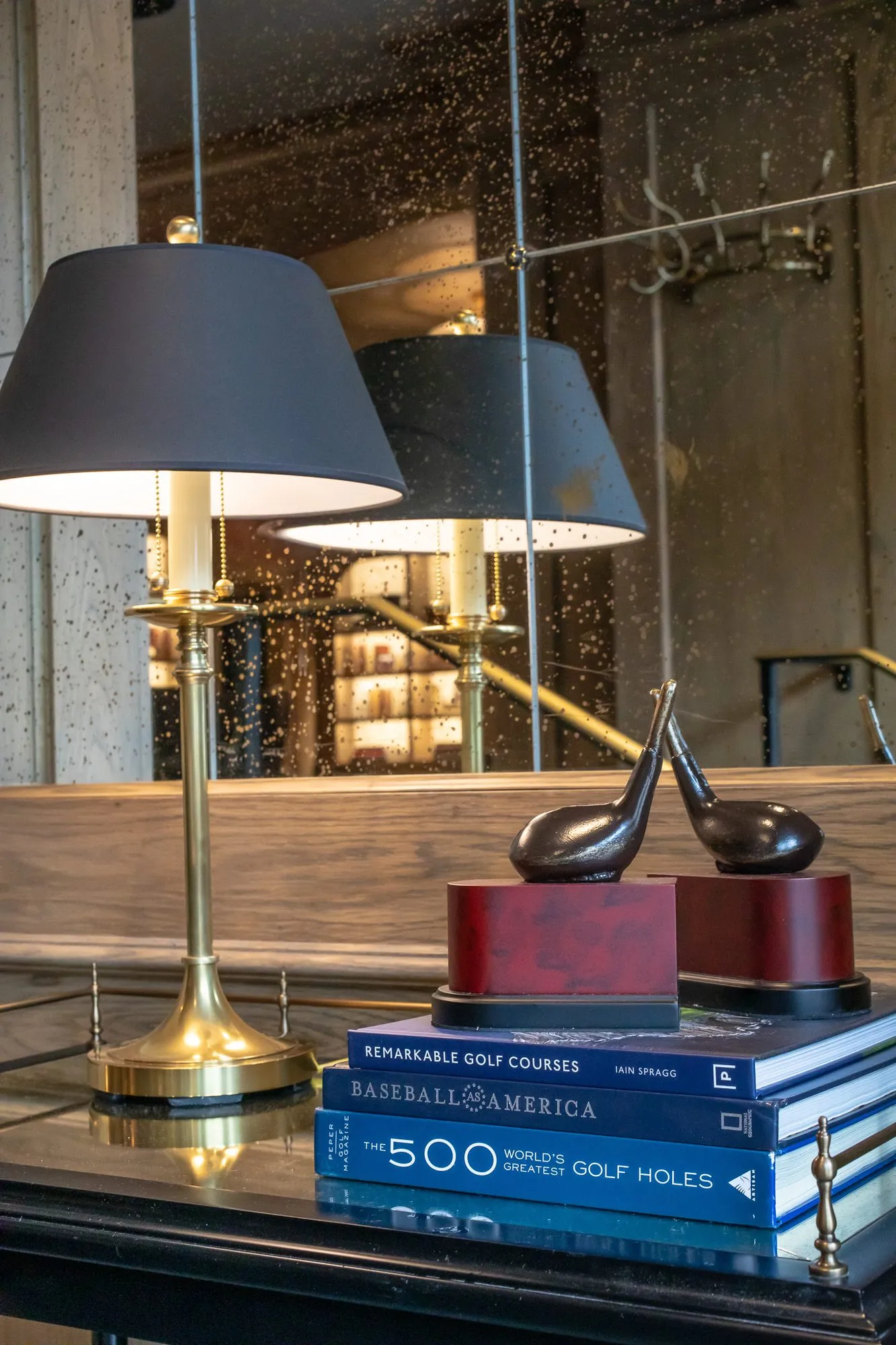 Private club interior detail: brass lamp beside golf club bookends and golf books on a dark table, antique mirror behind