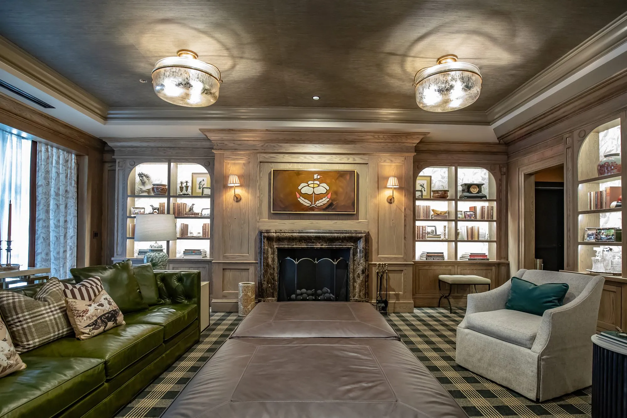 Private club library with a long upholstered ottoman between a green leather sofa and skirted armchair