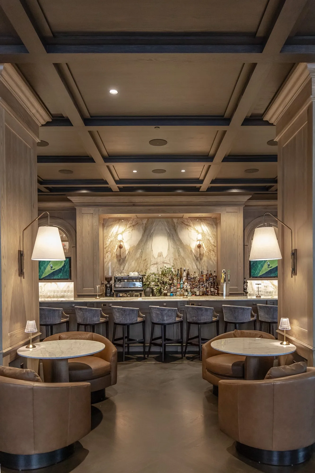 Private club bar: symmetrical view to the marble bar back, swing-arm lamps over paired leather tub chairs either side
