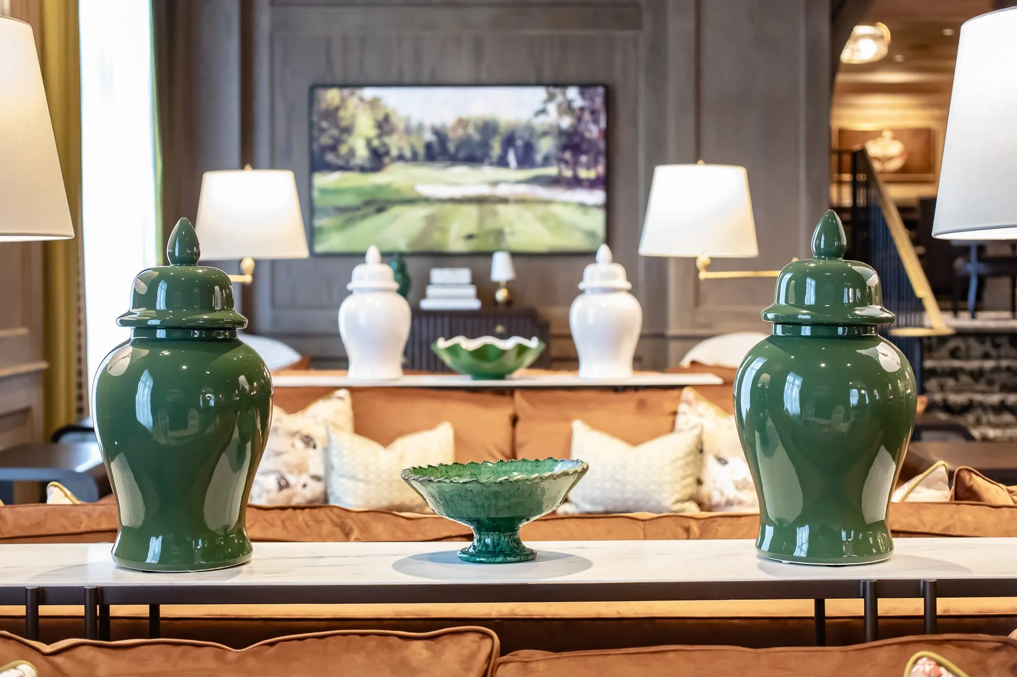 Private club interior detail: green ginger jars flanking a green glass bowl on a marble console, golf painting beyond