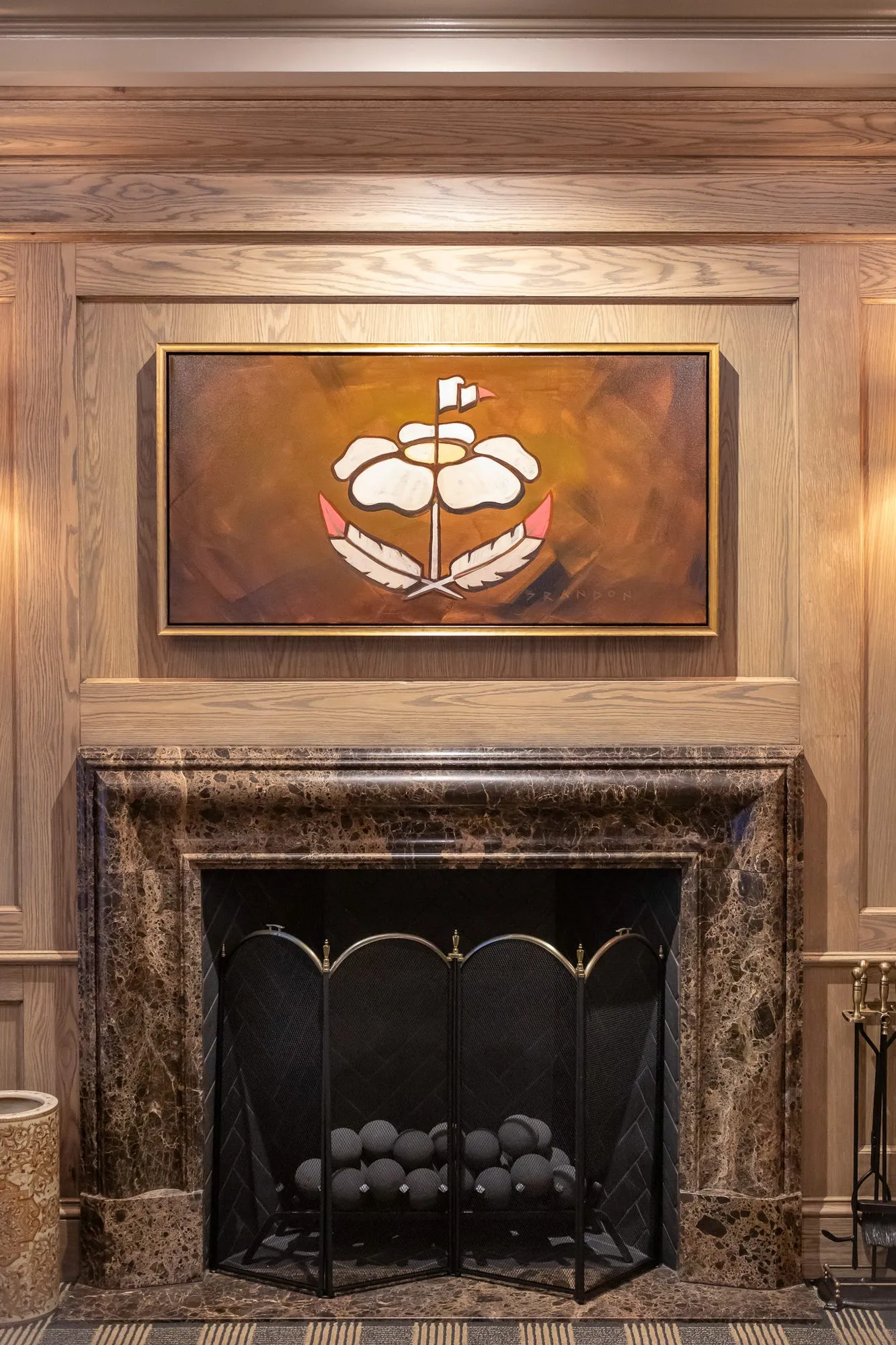 Private club interior detail: rose emblem painting above a dark marble fireplace with a brass fire screen