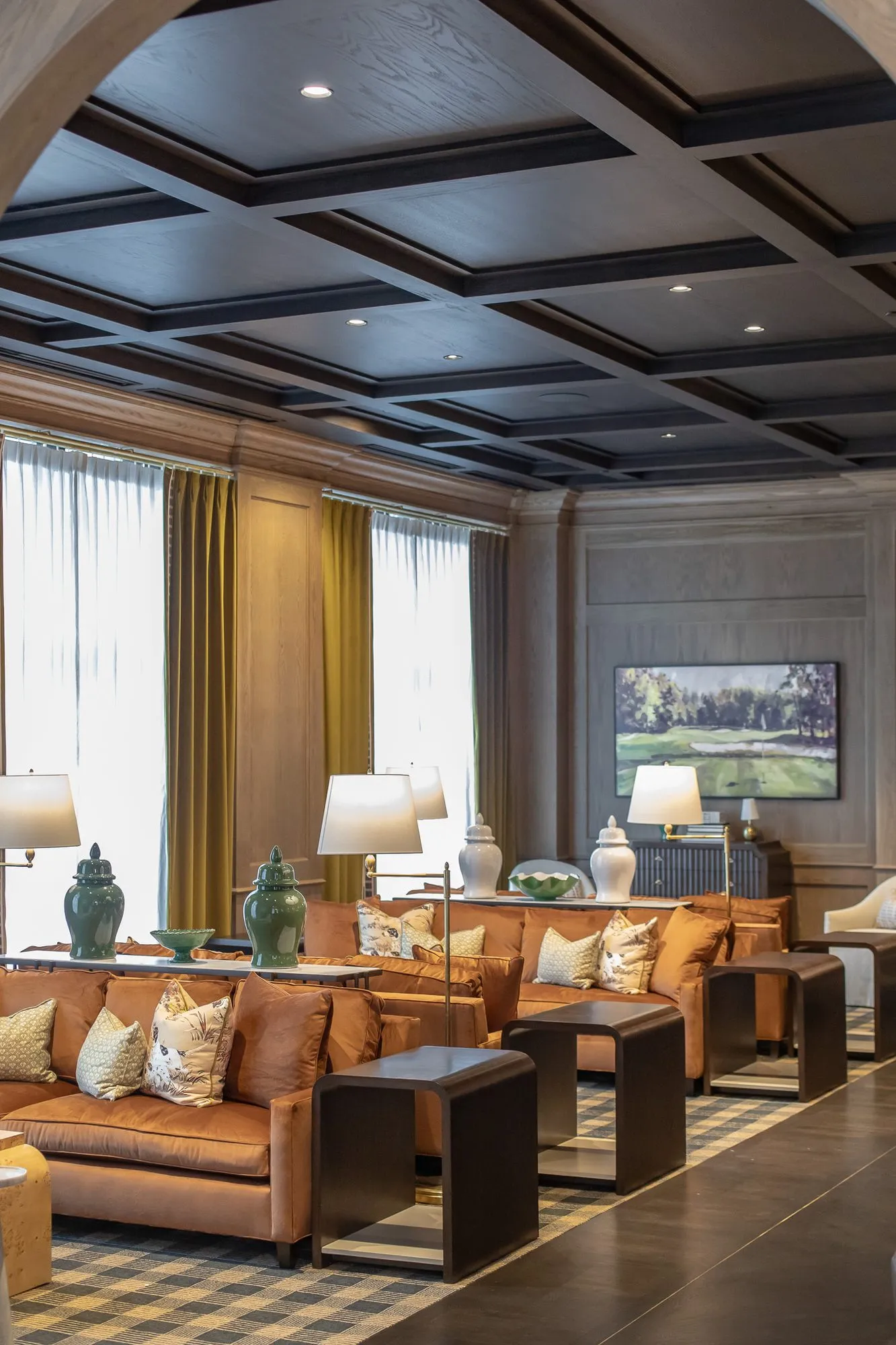 Private club lounge seen through an oak arch, cognac sofas along curtained windows below a coffered ceiling