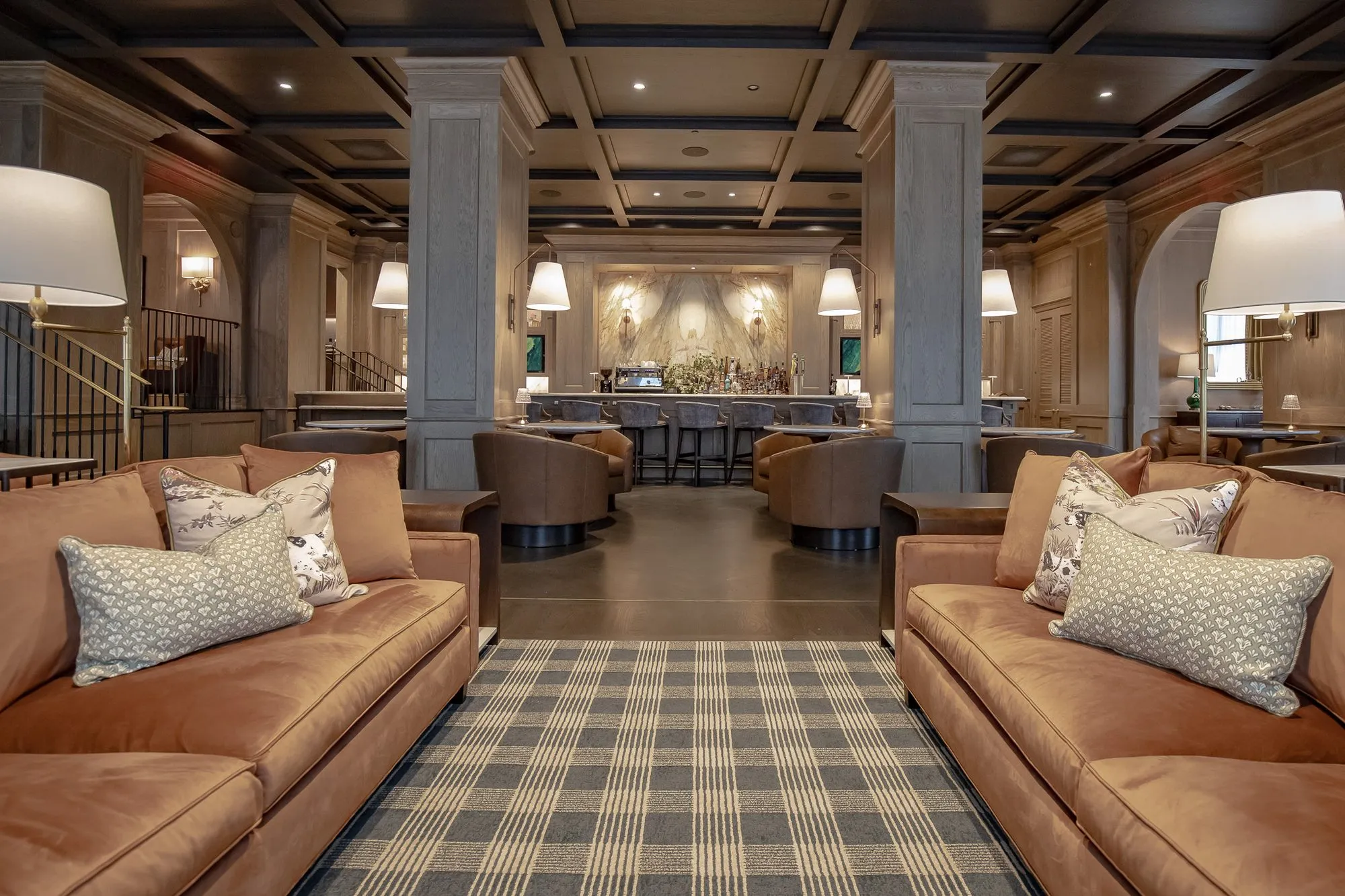 Private club lounge, a low view between cognac sofas with patterned pillows down the checked runner to the bar