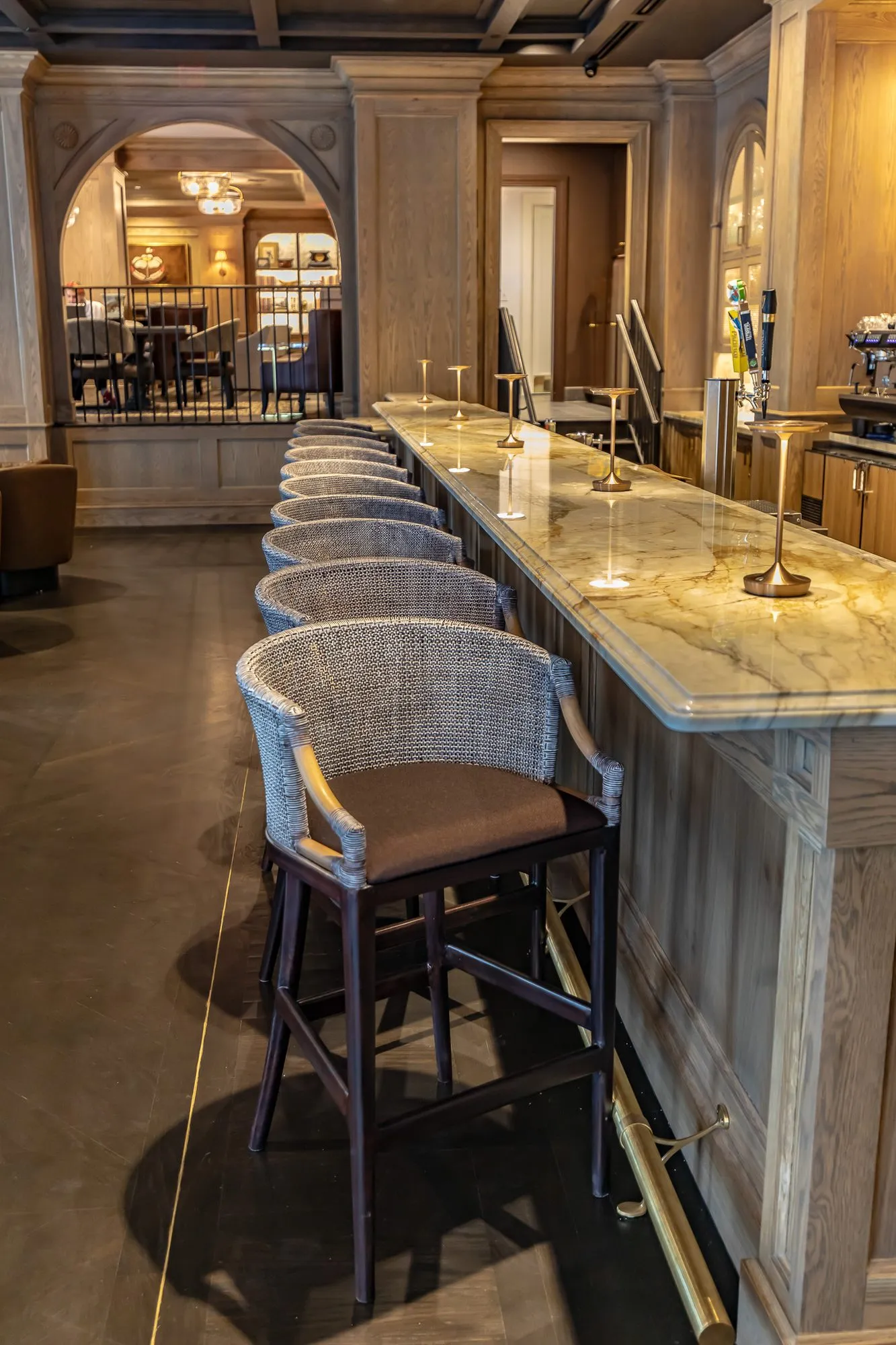 Private club bar: cane back stools with leather seats along the marble bar, brass foot rail below