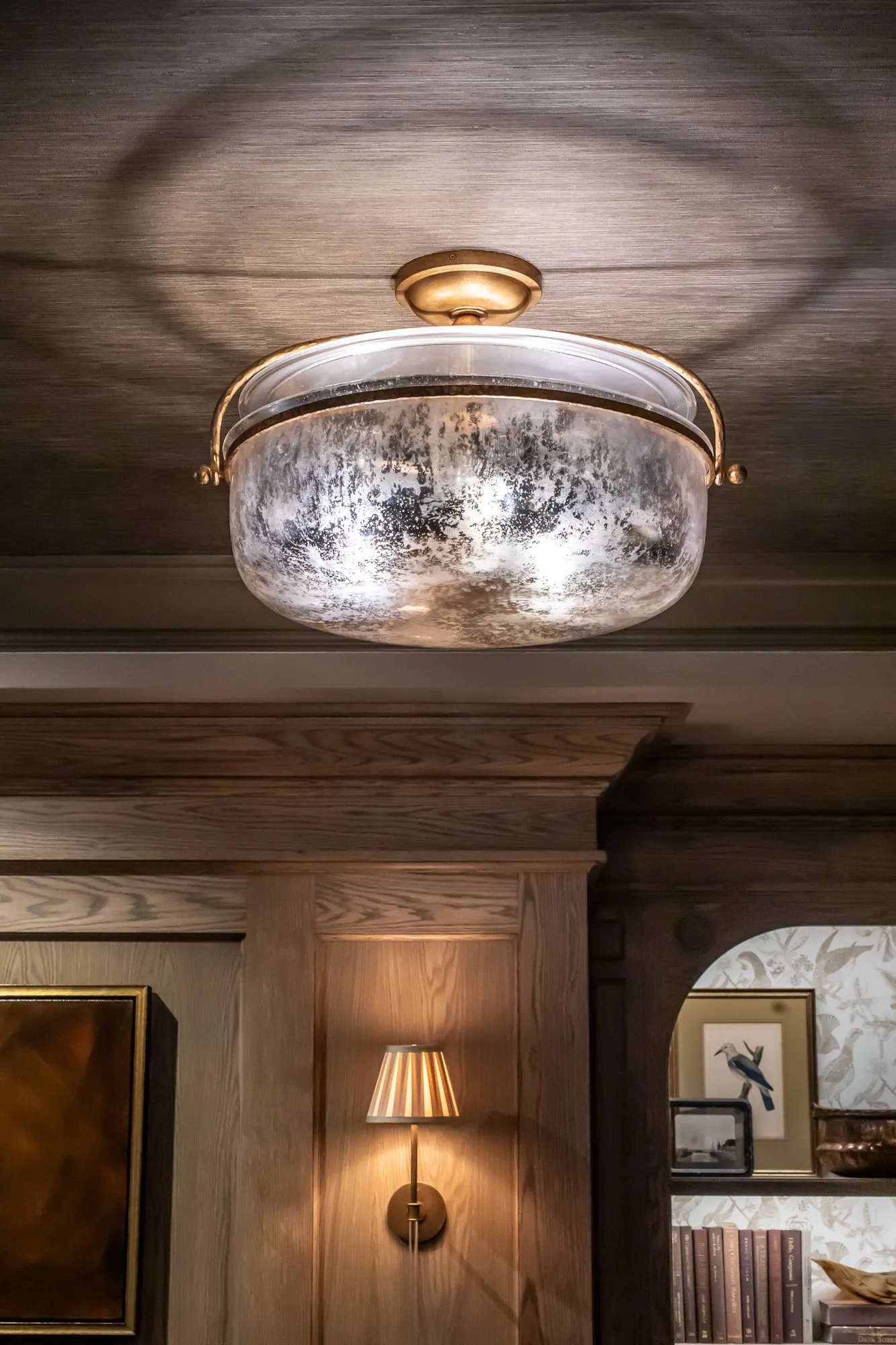 Private club interior detail: mercury glass flush ceiling light above oak panelling and a pleated sconce