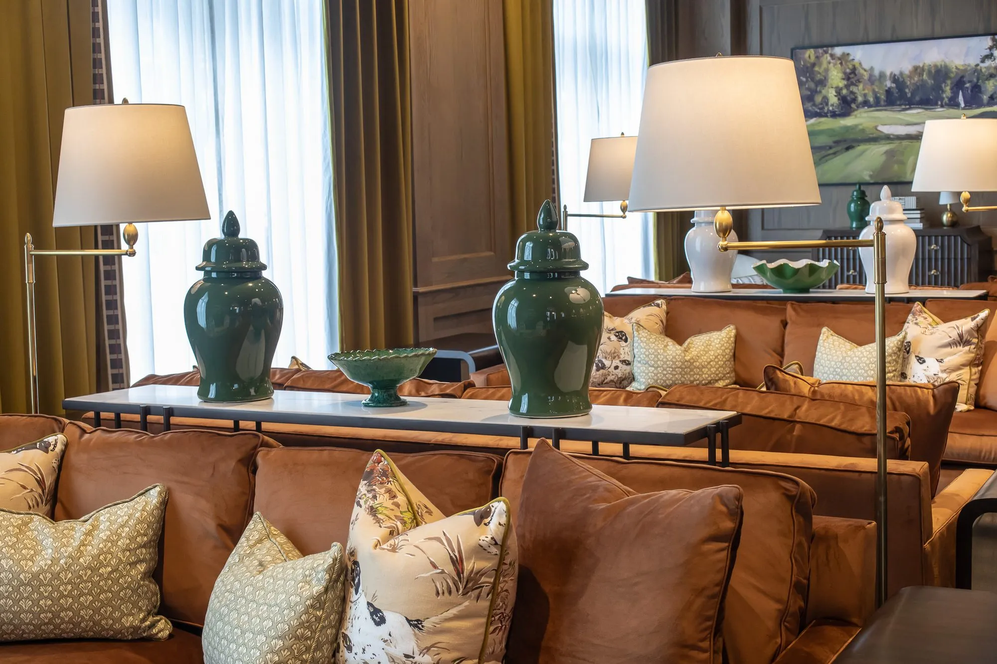 Private club interior detail: green ginger jars on the console behind cognac sofas, swing-arm floor lamps either side