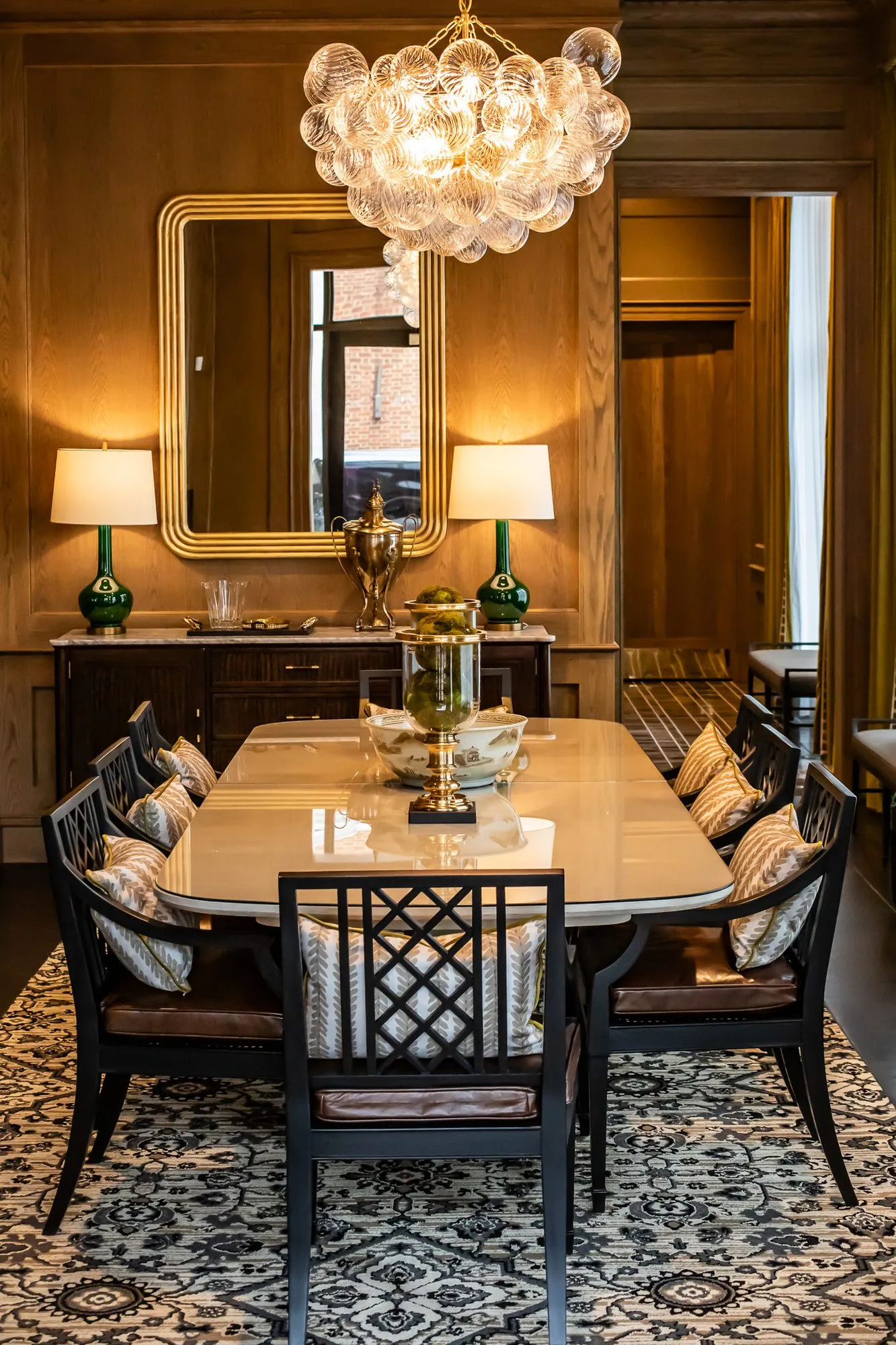 Private club dining room, looking down the table under the bubble glass chandelier to a gilt mirror flanked by green lamps