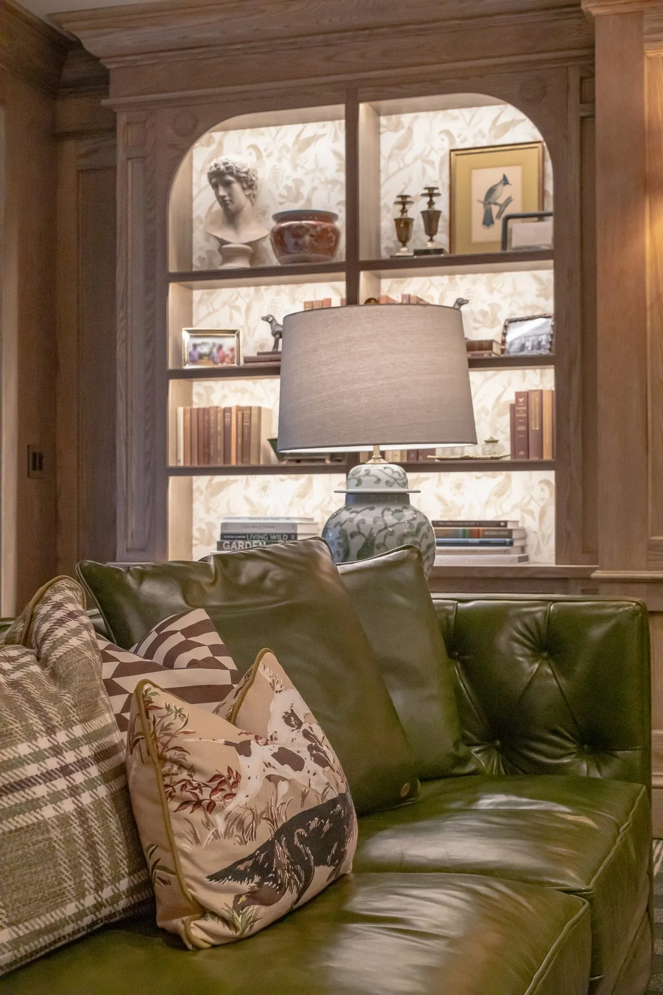 Private club interior detail: green leather sofa with patterned pillows before an arched lit bookcase with a classical bust
