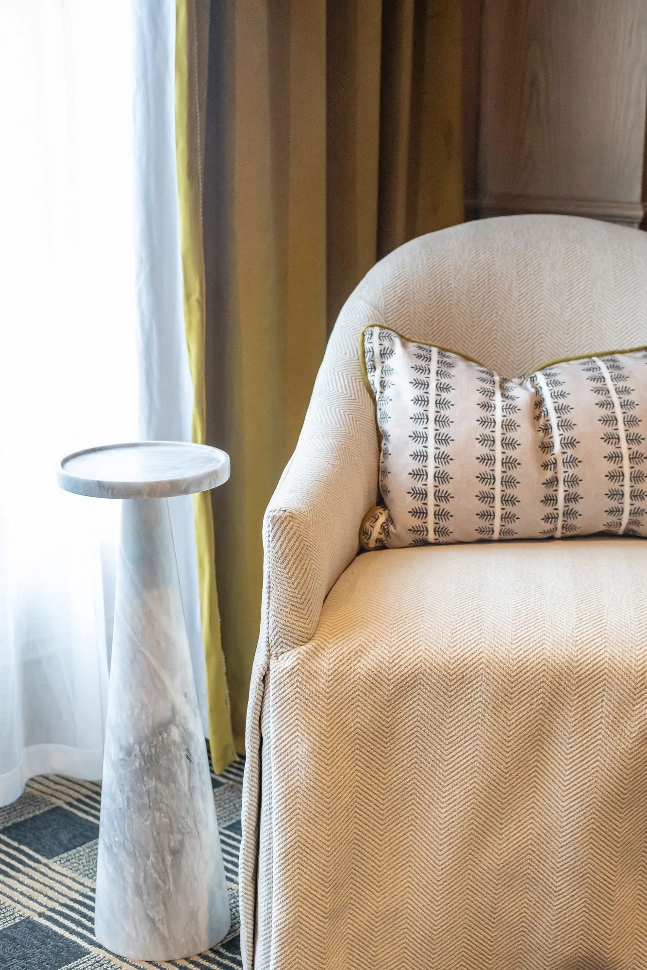 Private club interior detail: slipcovered armchair with a patterned pillow beside a white marble pedestal side table