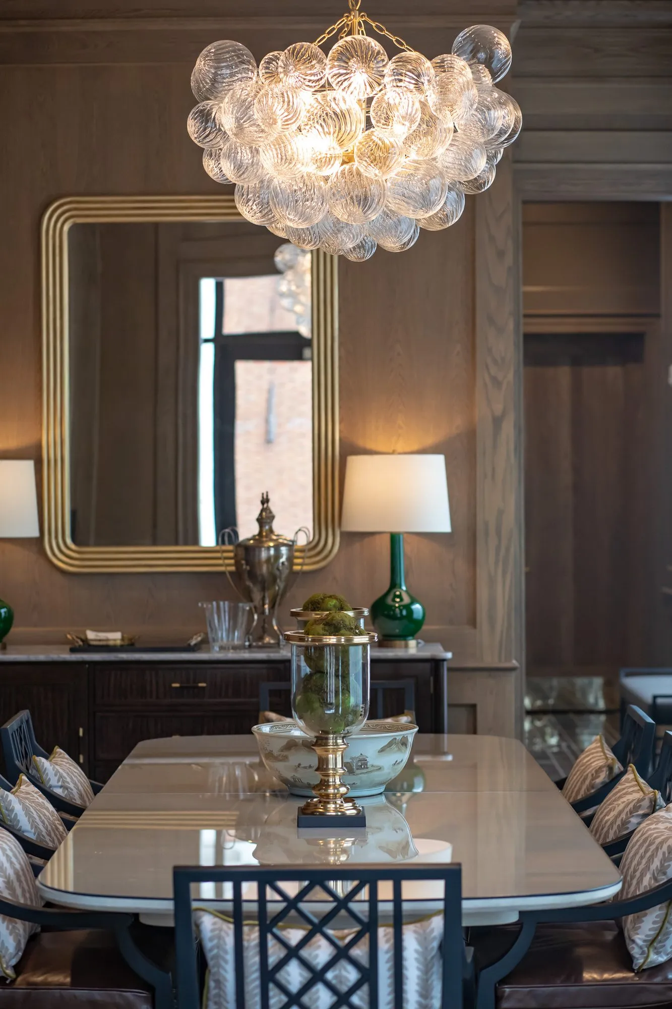 Private club interior detail: bubble glass chandelier above a brass urn centrepiece, gilt mirror behind