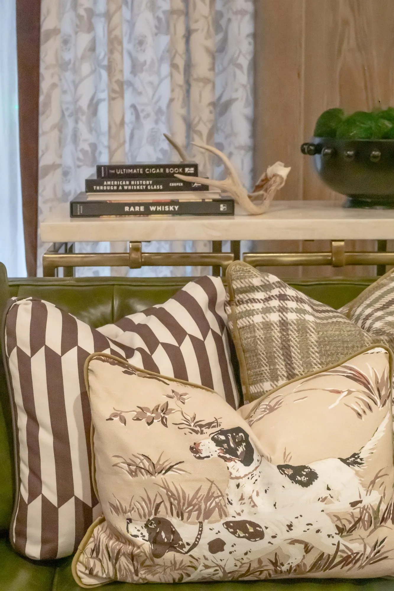 Private club interior detail: pointer dog print pillow with striped and plaid pillows, books and antlers on a console behind
