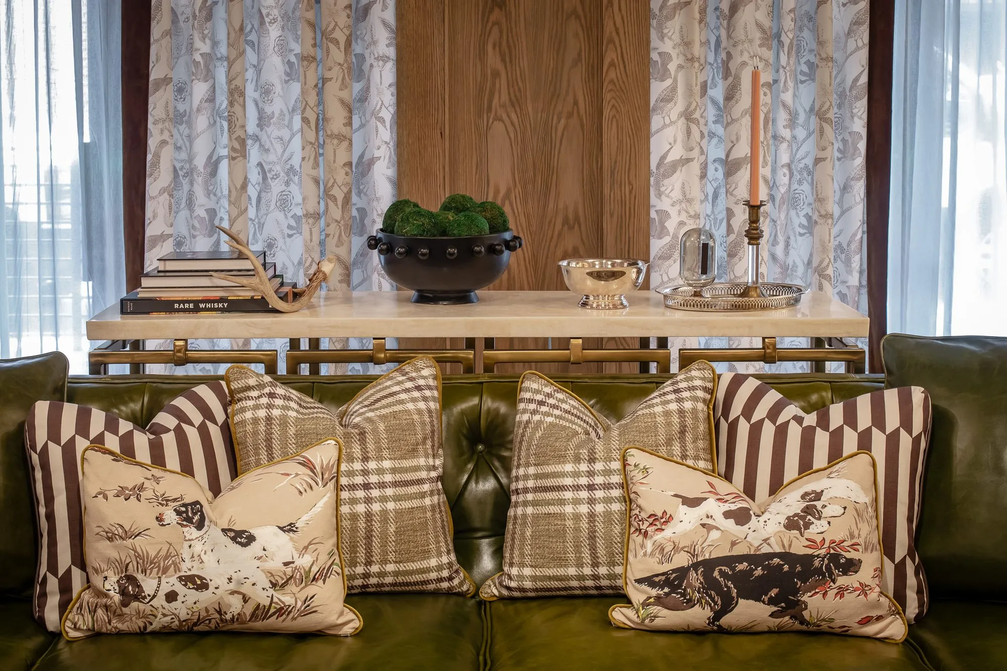 Private club interior detail: green tufted leather sofa with dog print, plaid and striped pillows below a long console
