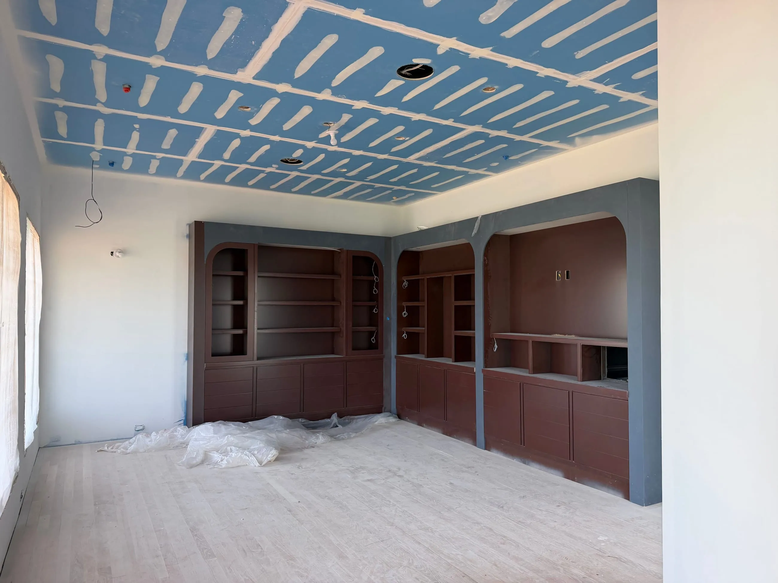 Private club clubhouse under construction: room of arched dark stained built-in shelving and cabinetry below a taped ceiling