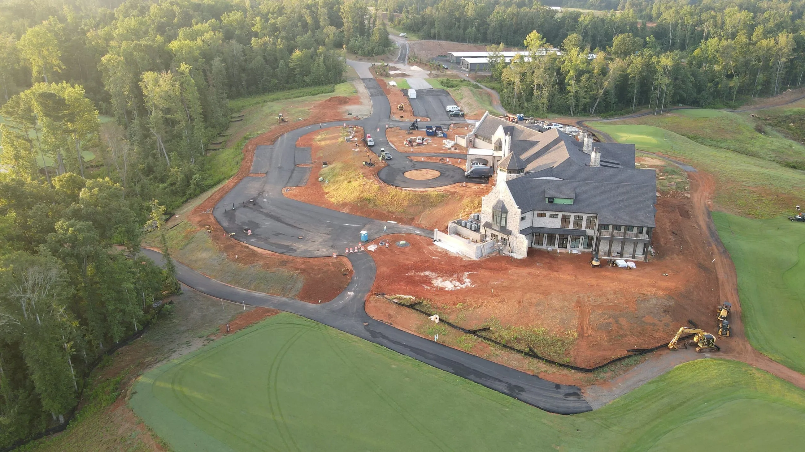 Private club clubhouse under construction: aerial view over graded red clay ground, freshly laid paving and the fairway
