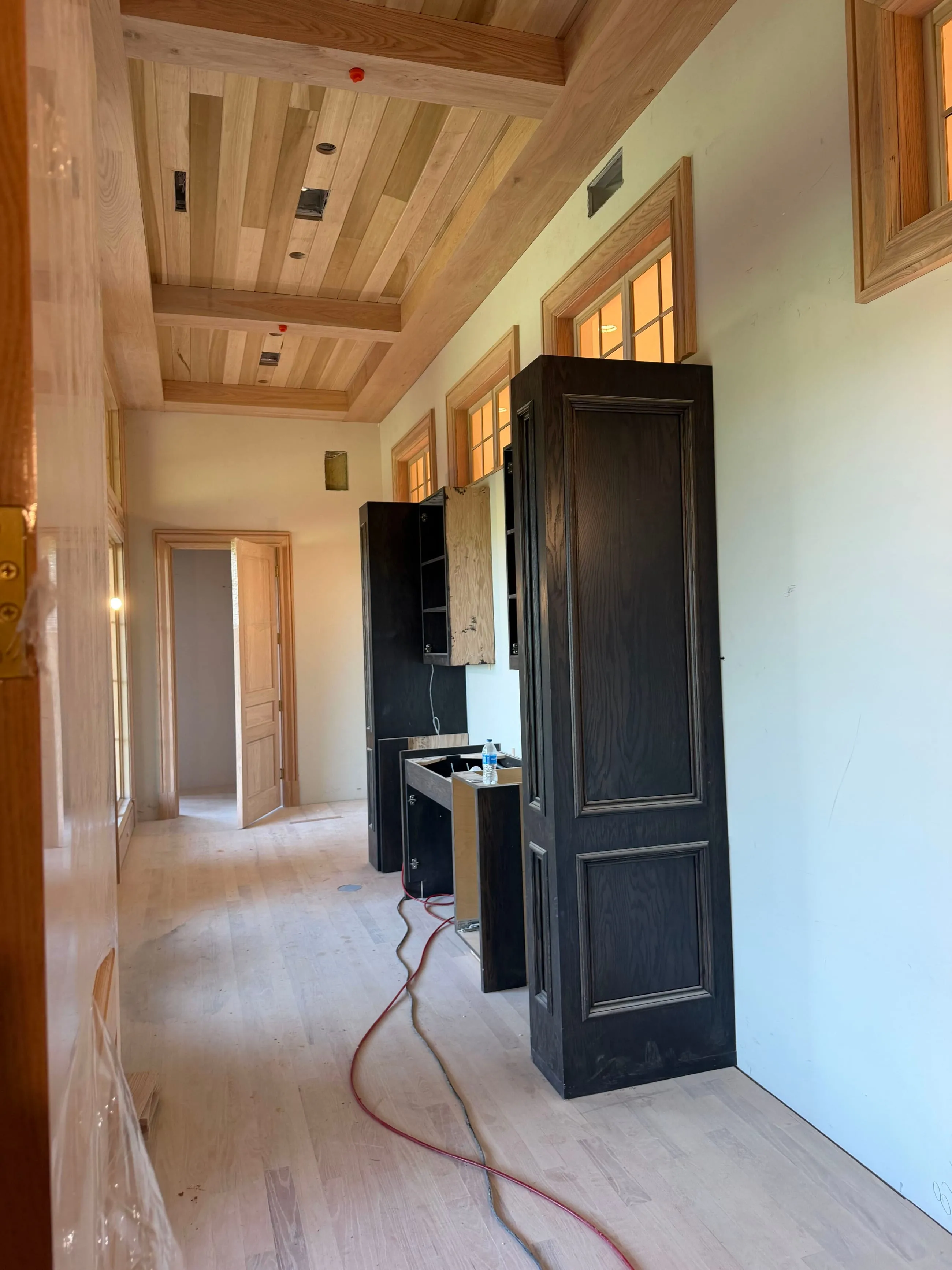 Private club clubhouse under construction: dark cabinetry going in along a room with a beamed wood plank ceiling and transoms