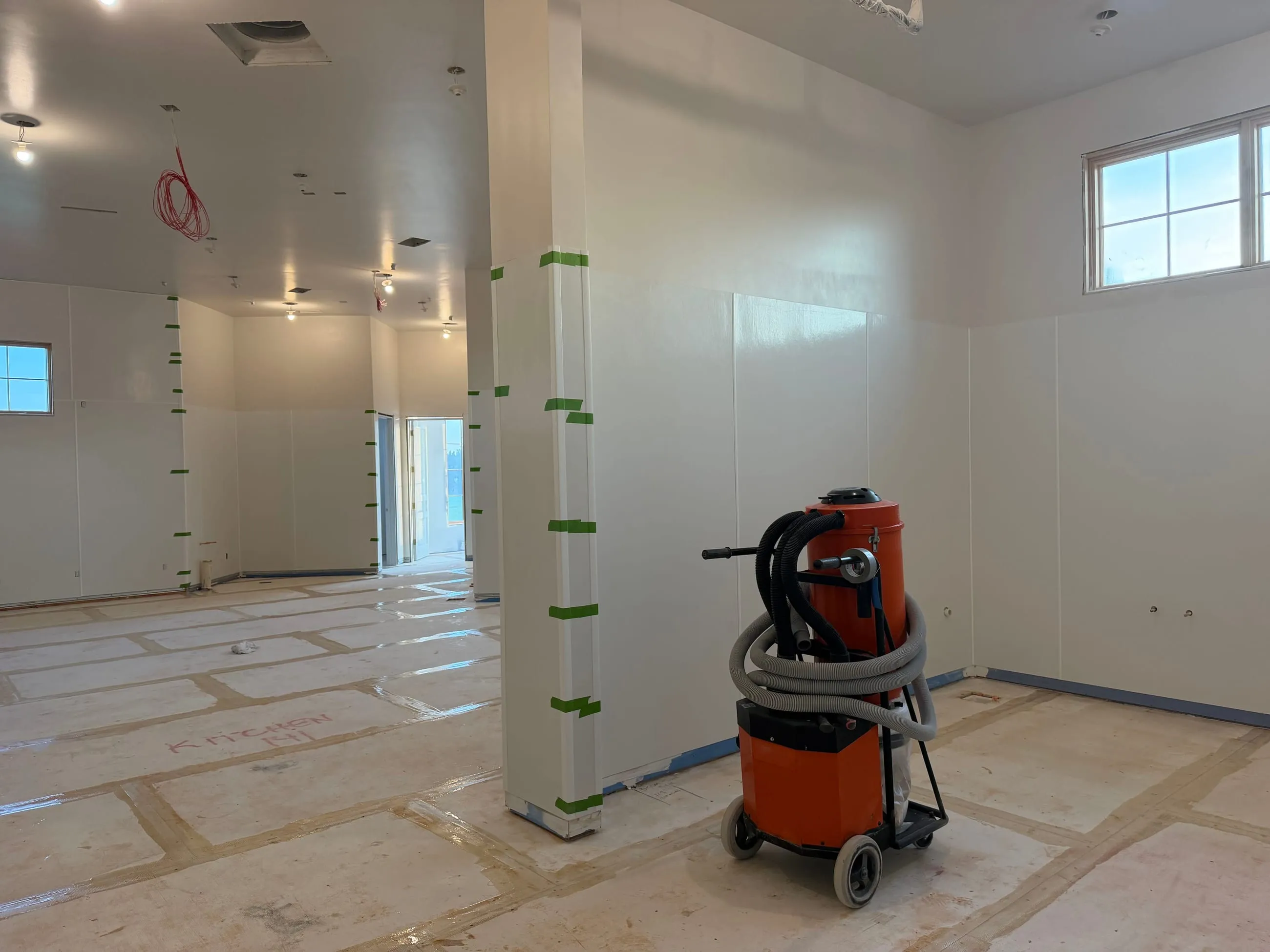 Private club clubhouse under construction: white-panelled room with taped corner guards and an orange dust extractor