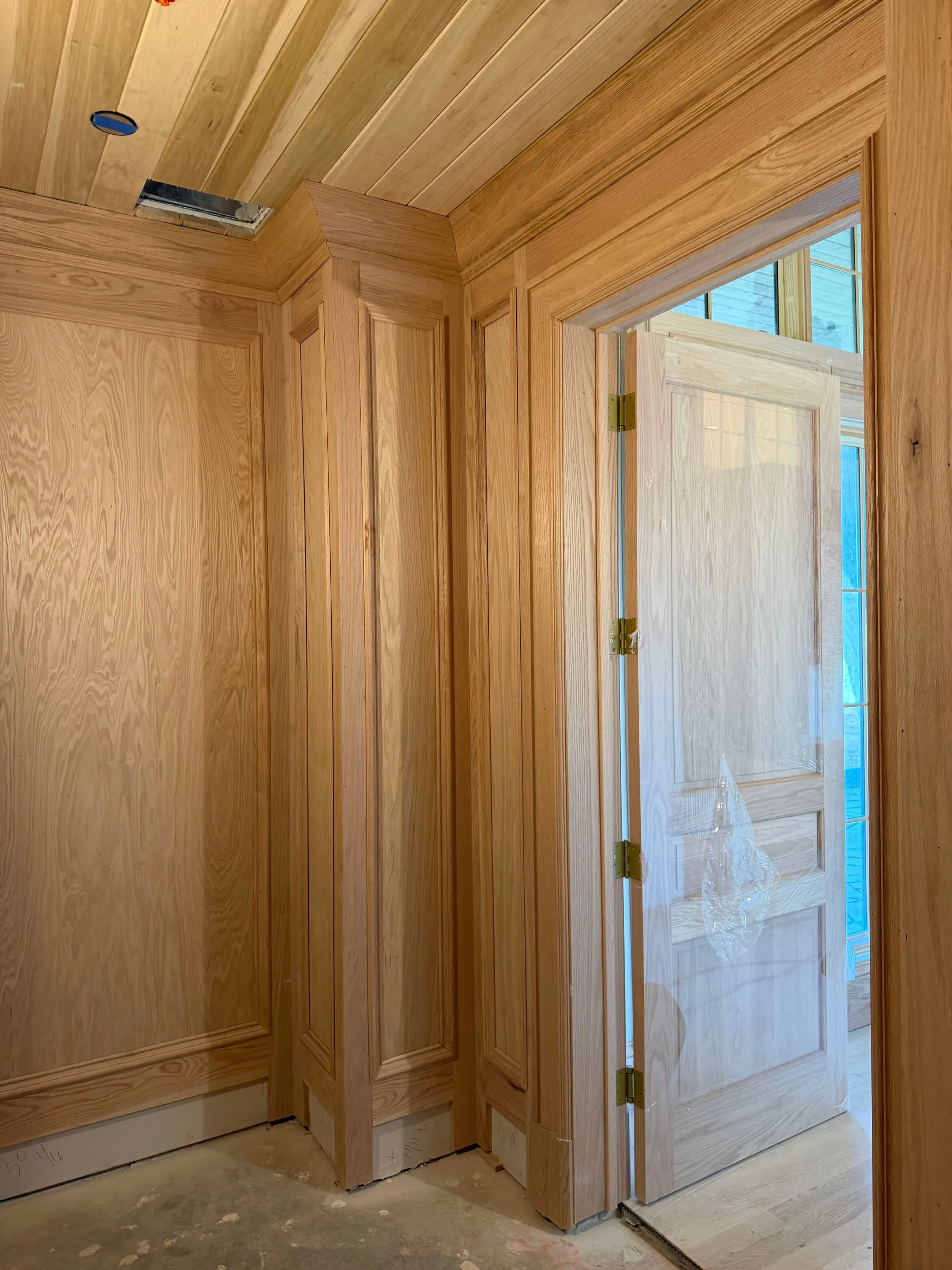 Private club clubhouse under construction: oak-panelled hall with a panelled oak door below a plank ceiling, the floor bare