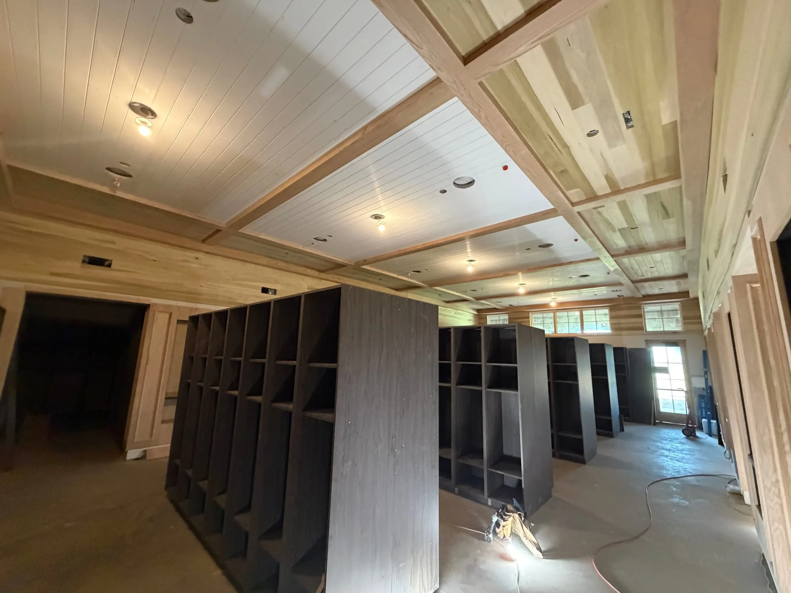 Private club clubhouse under construction: locker room with dark locker bays below a coffered wood and plank ceiling