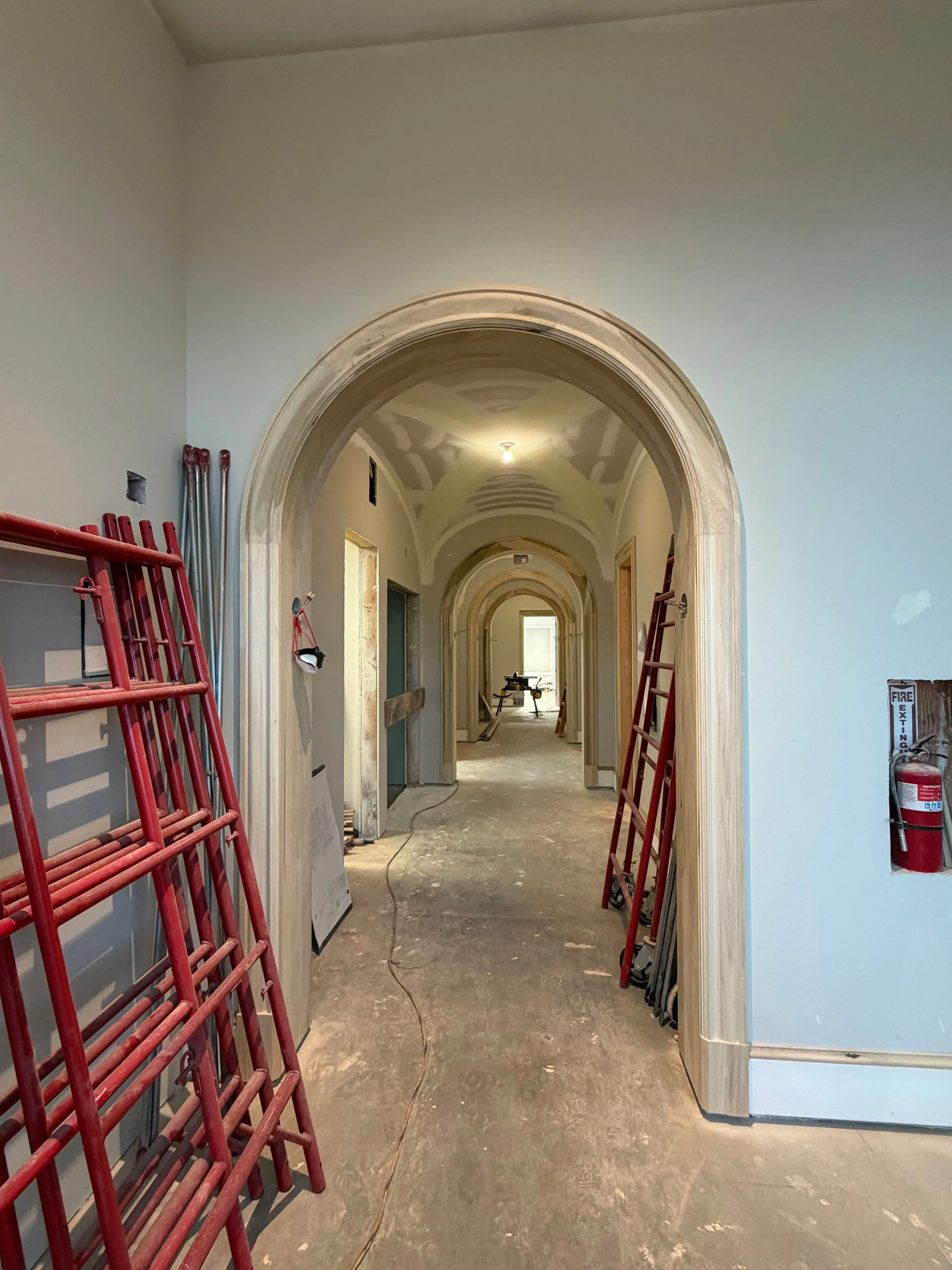 Private club clubhouse under construction: arched corridor with its millwork casings installed, ladders and tools in place