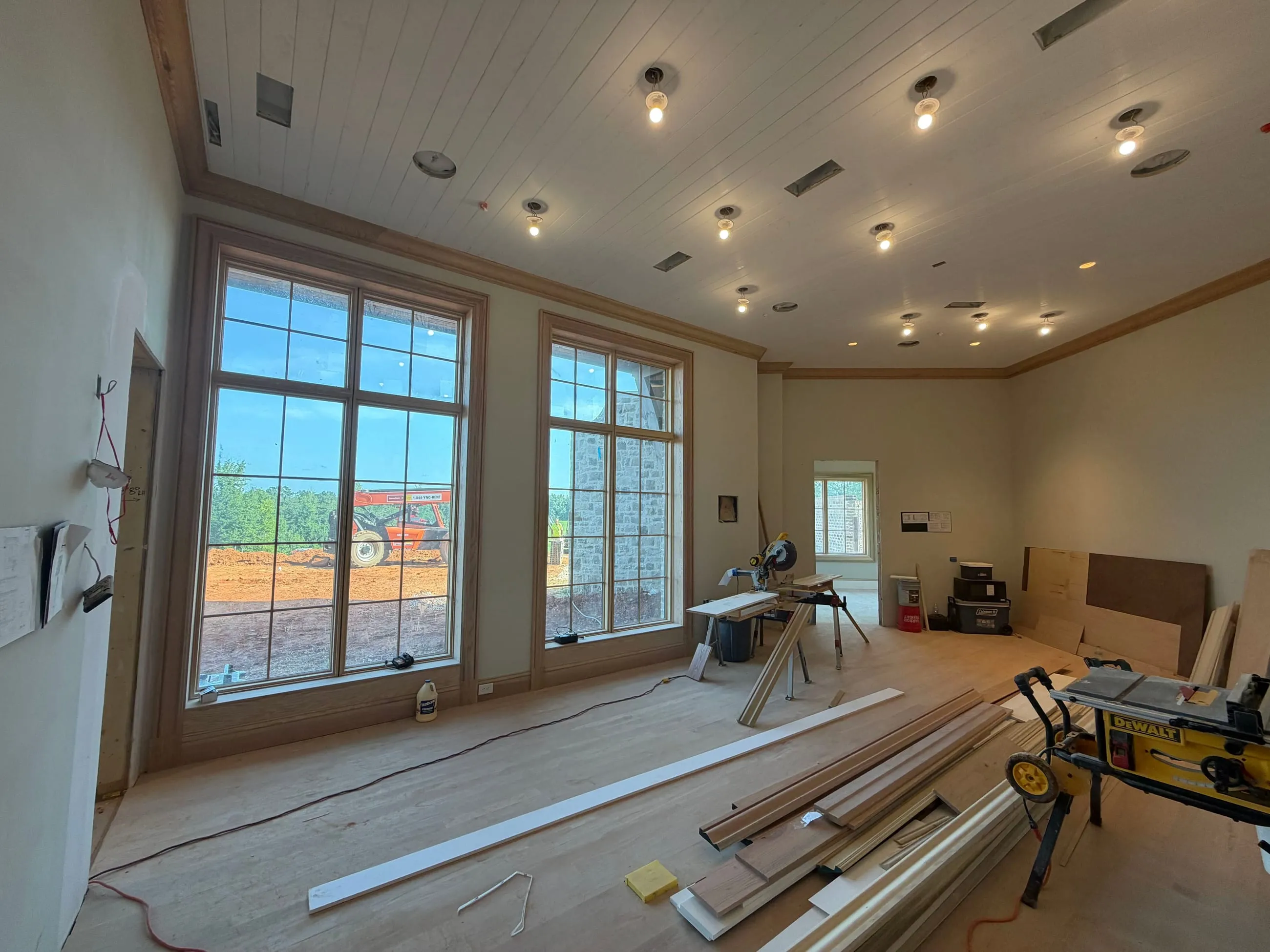 Private club clubhouse under construction: room with tall windows and a white plank ceiling, trim boards and a table saw