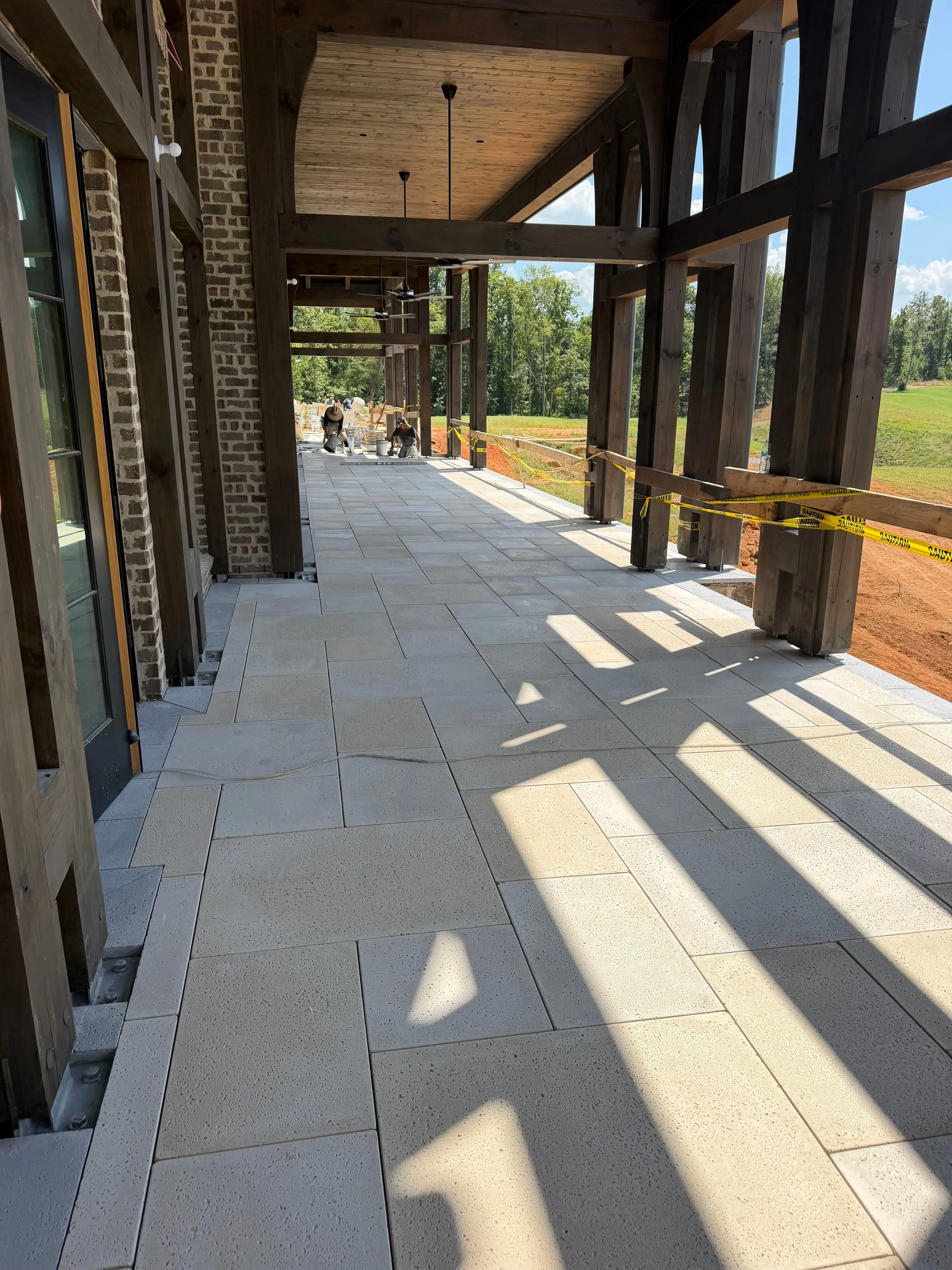 Private club clubhouse under construction: covered veranda with stone paving laid between timber columns, the course beyond