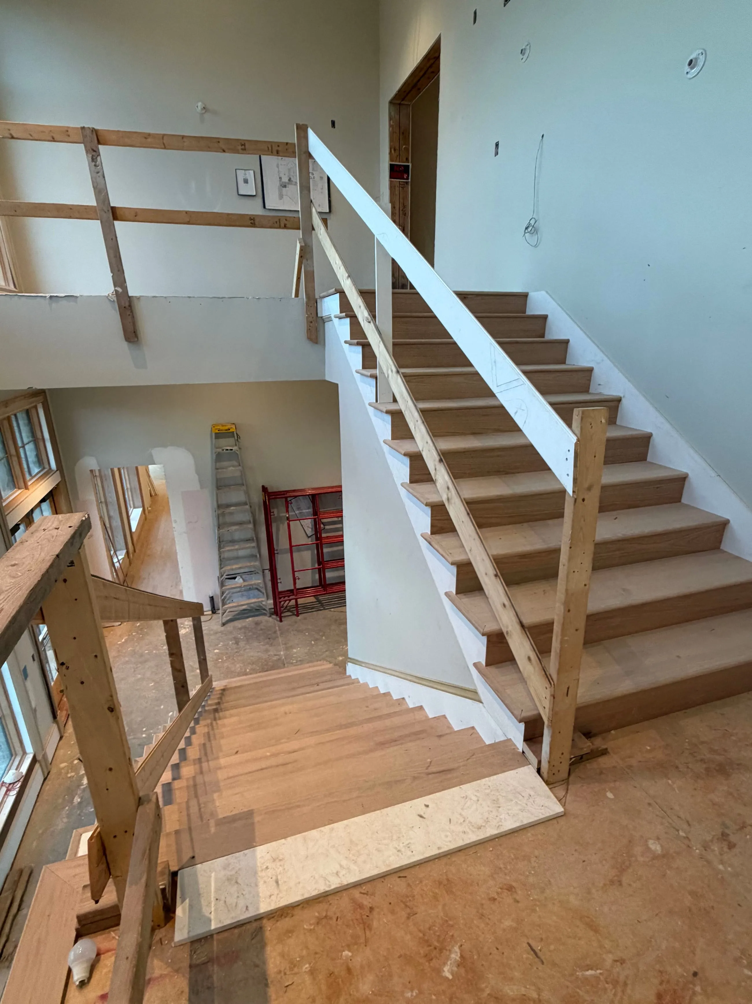 Private club clubhouse under construction: stair with oak treads installed behind temporary timber rails, a plastered wall