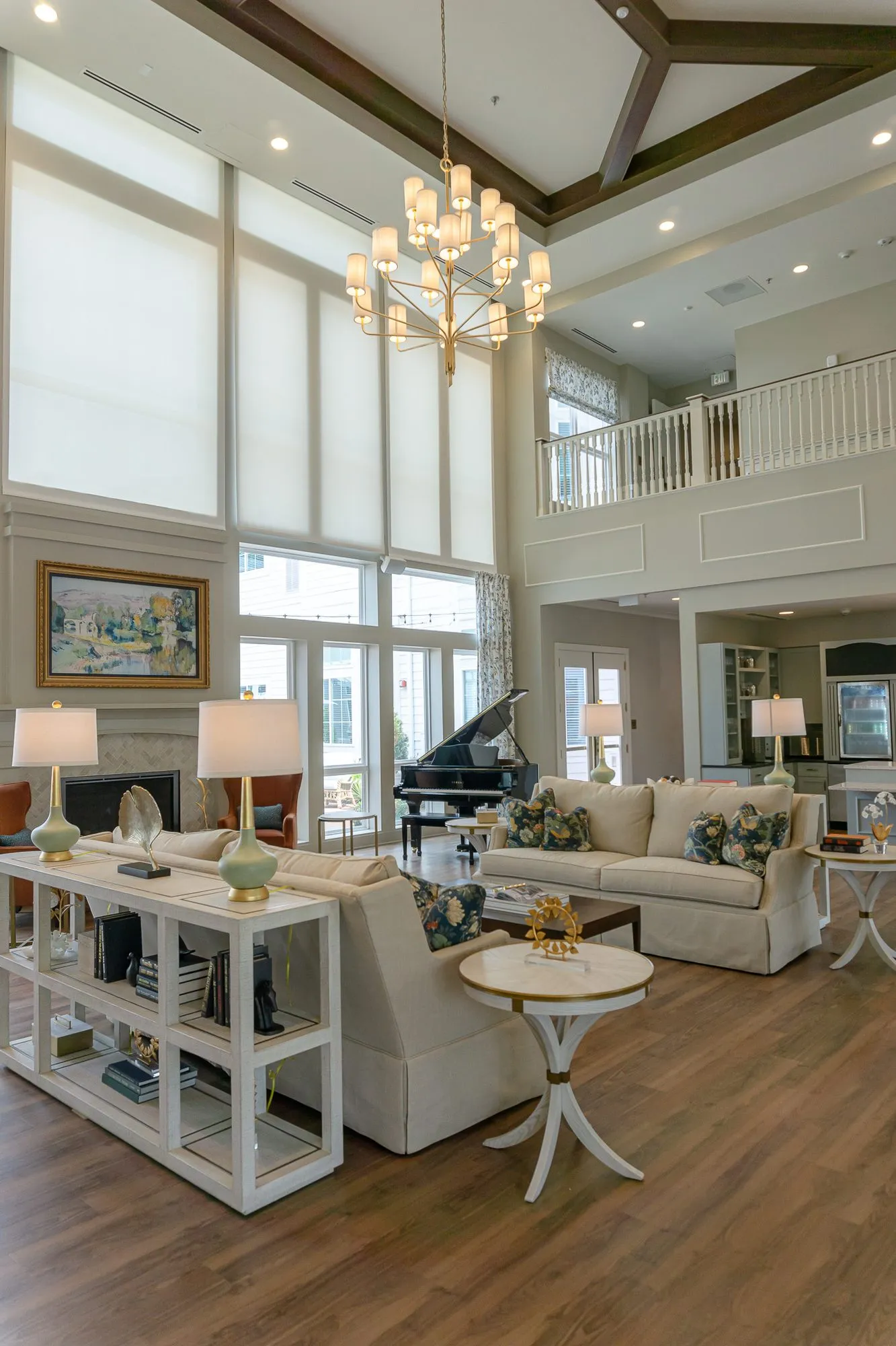 Senior living double-height great room with a tiered chandelier above a cream sofa, a grand piano and the balcony beyond