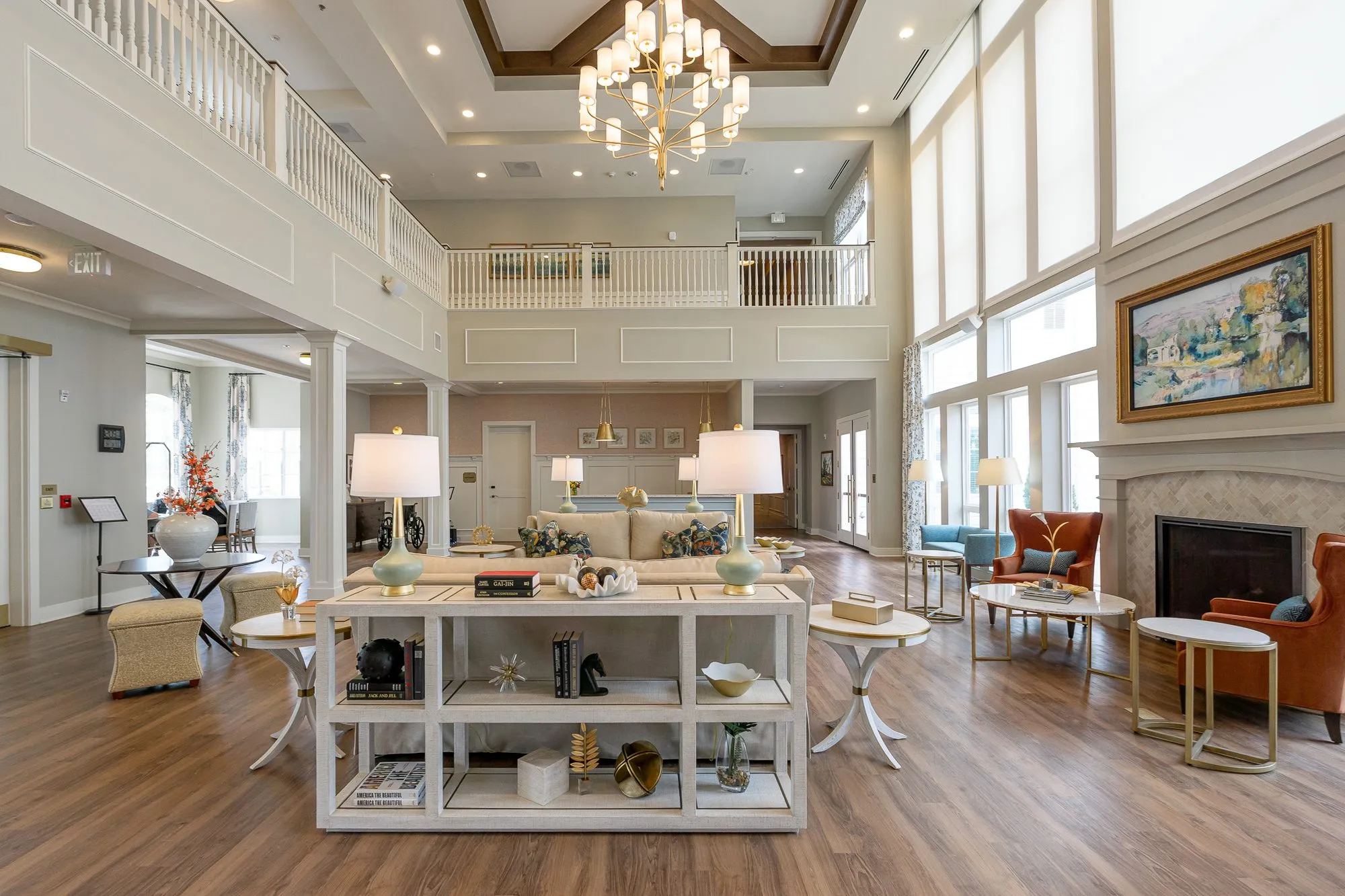 Senior living great room with a white open shelf console, a tiered chandelier and a stone fireplace below the balcony