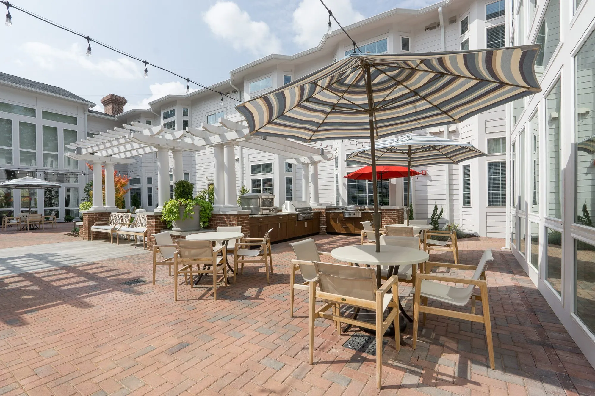 Senior living courtyard with string lights over dining tables, white pergolas and the outdoor kitchen along the far side