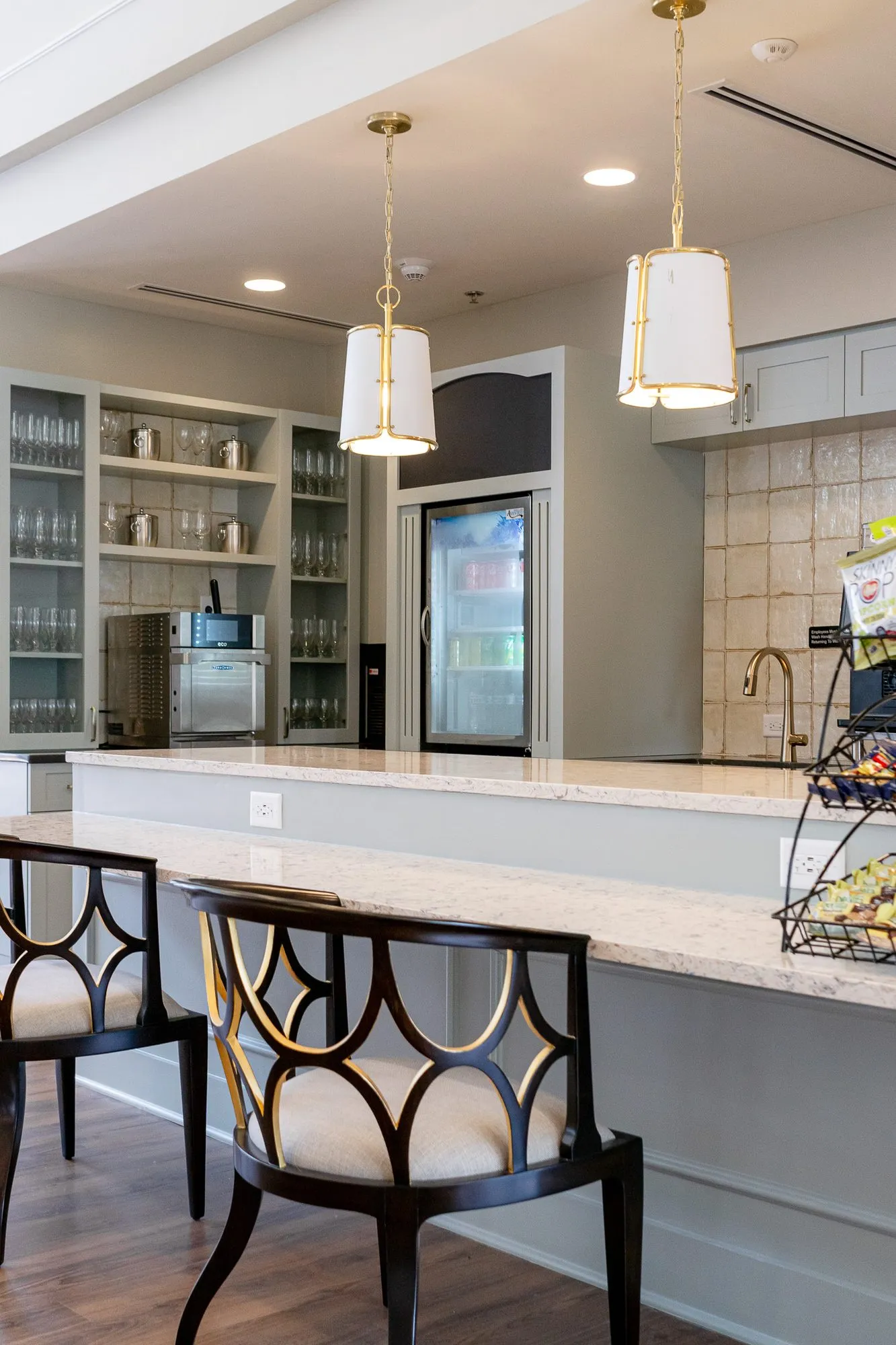 Senior living kitchen with fretwork back counter chairs at the stone counter, a snack rack and glass-front cabinets