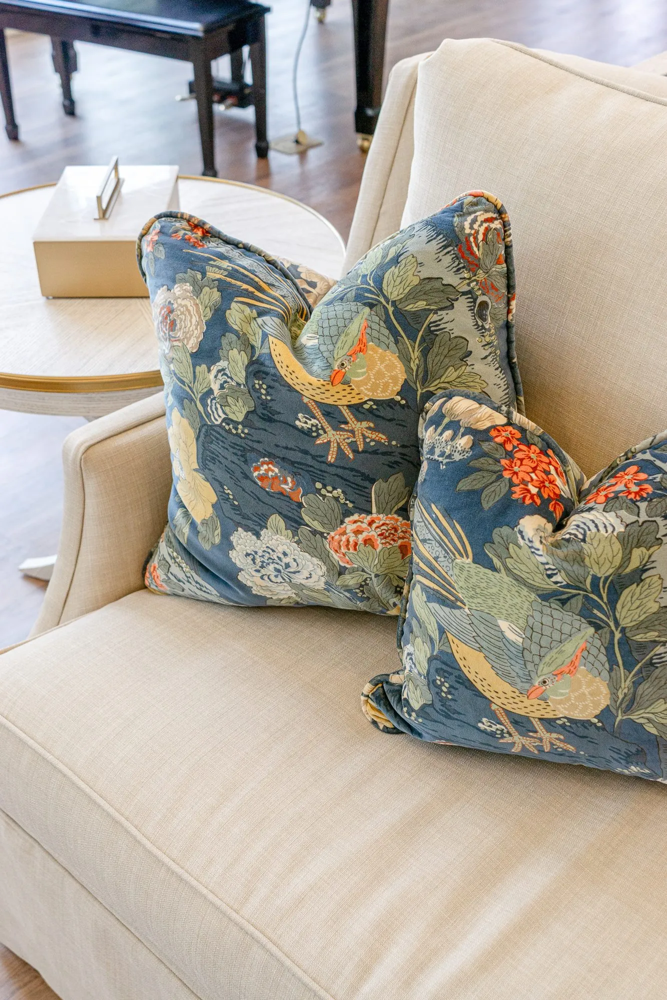 Senior living interior detail: navy pillows printed with birds and flowers on a cream sofa, a piano bench behind