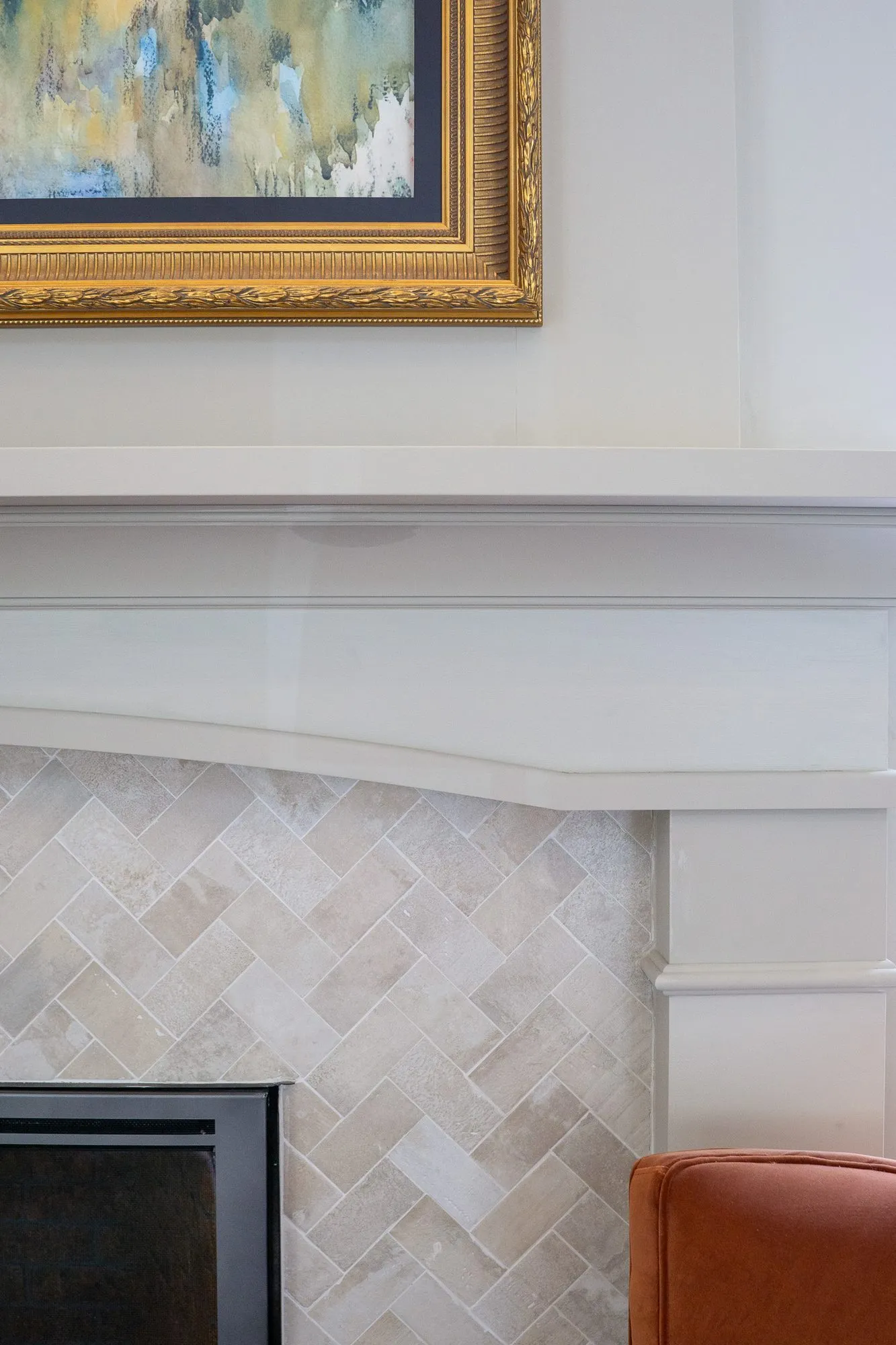 Senior living interior detail: cream fireplace mantel with a herringbone stone tile surround under a gilt-framed painting