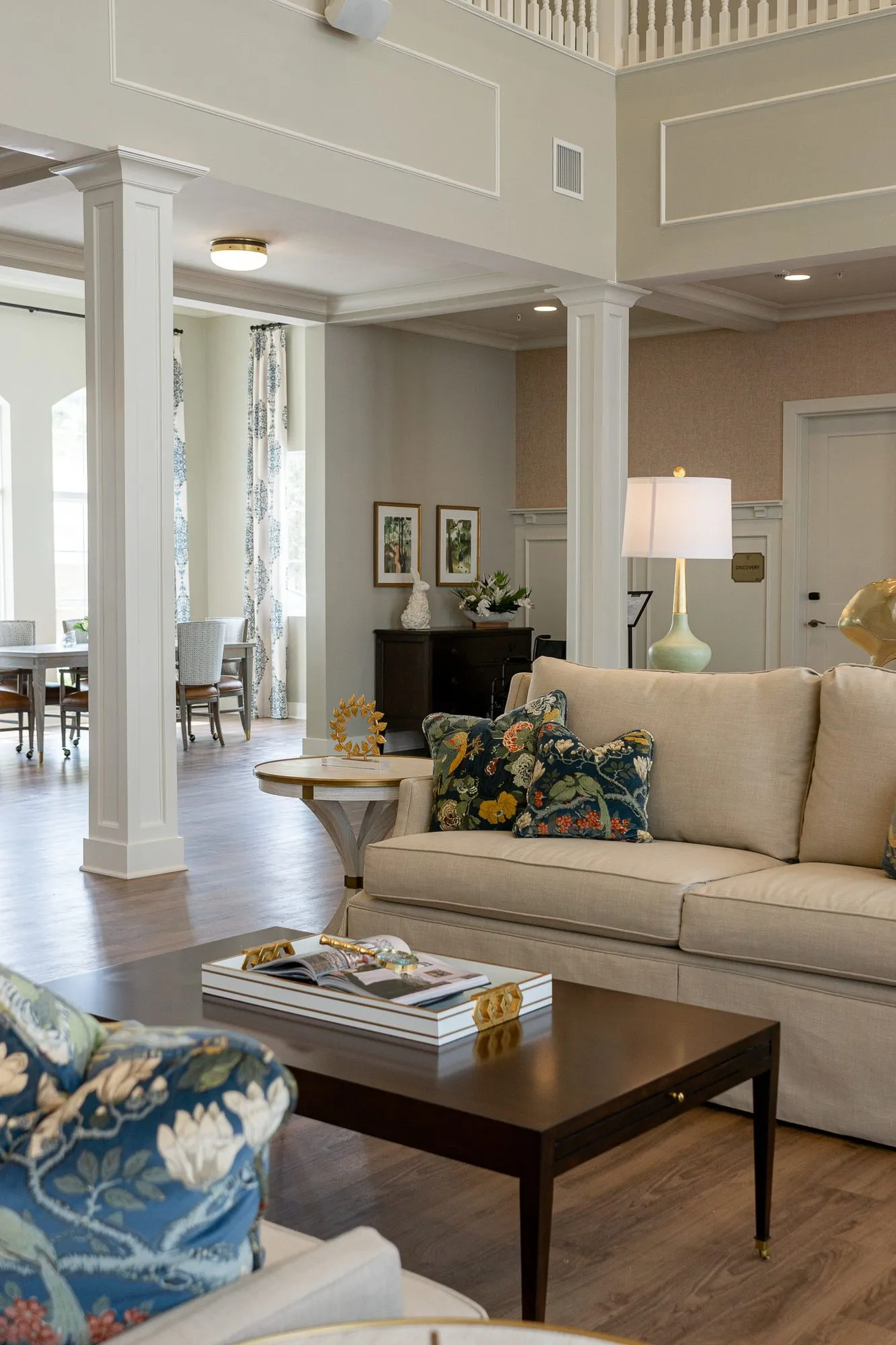 Senior living seating area with a cream sofa and dark coffee table between white columns, a blue floral armchair in front
