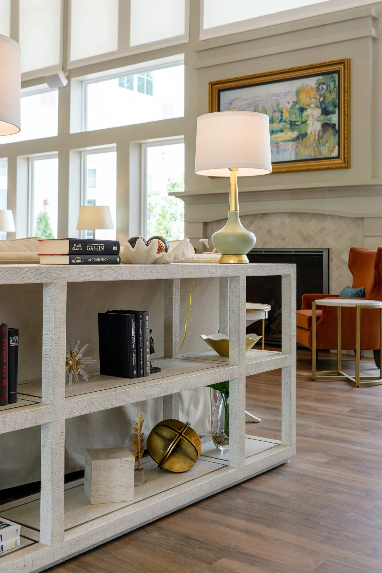 Senior living great room with a white open shelf console behind a sofa, a gilt-framed painting above the fireplace beyond