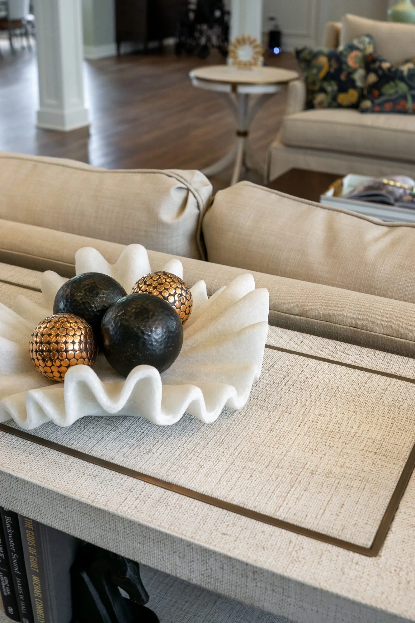 Senior living interior detail: white ruffled bowl holding black and copper spheres on a linen console behind the sofa