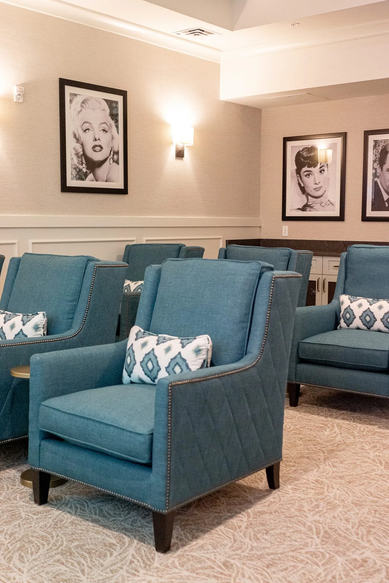 Senior living theater with blue quilted armchairs below framed black and white film star portraits