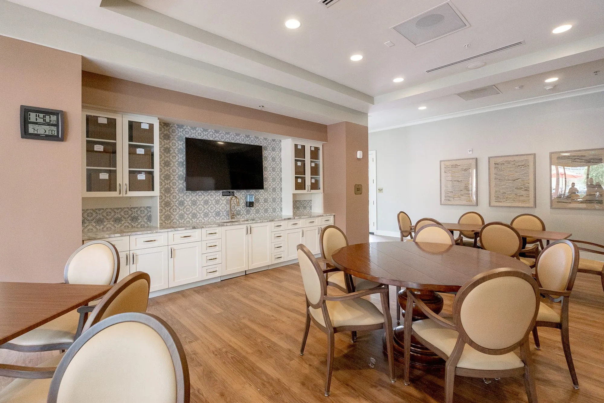 Senior living activity room with cream oval-back chairs at round tables, white cabinetry, patterned tile and a screen
