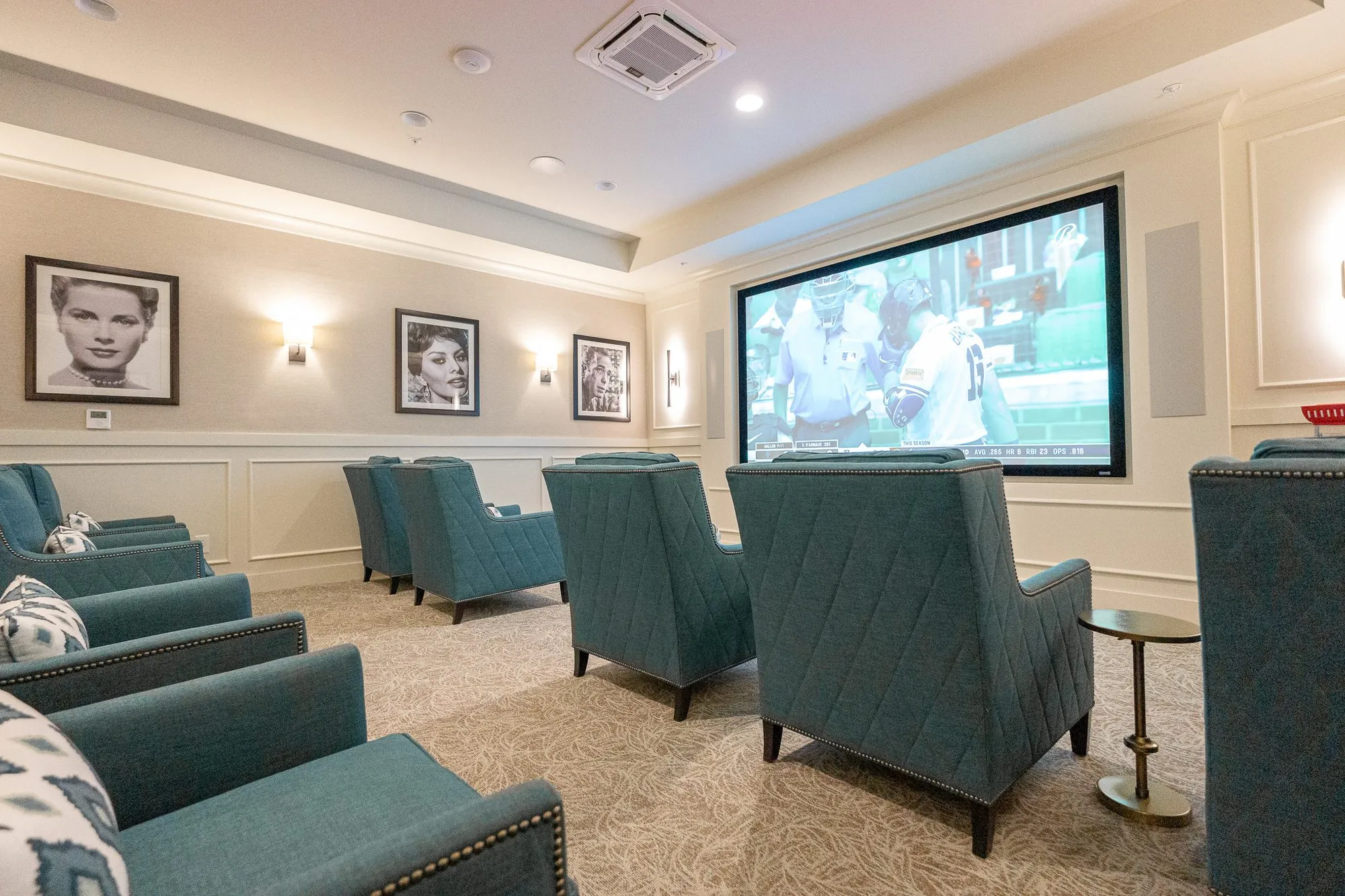 Senior living theater from the back row, teal armchairs facing a large screen between framed black and white portraits