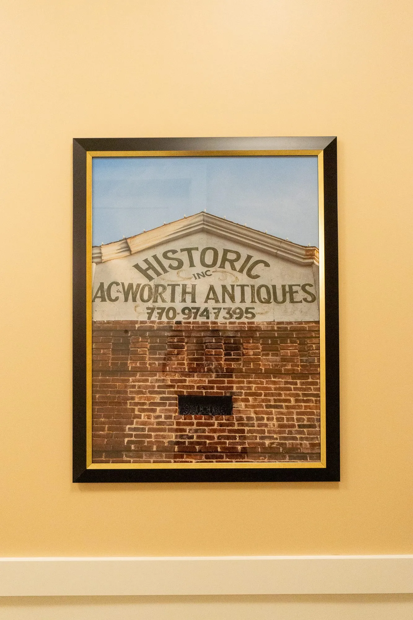 Senior living interior detail: framed photograph of a faded painted sign for an antiques shop on an old brick wall