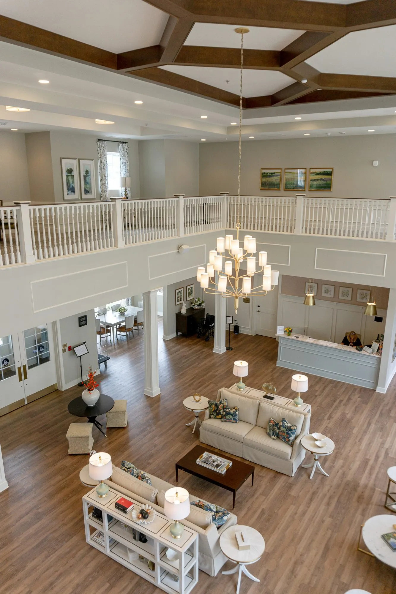 Senior living great room from the balcony, sofas, consoles and the reception desk under the tiered chandelier