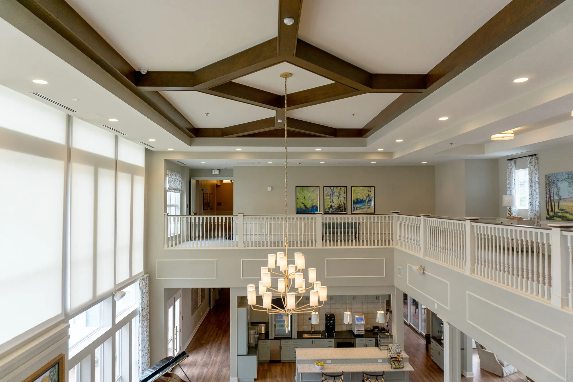 Senior living double-height great room, a tiered chandelier hanging from the beamed ceiling above the kitchen