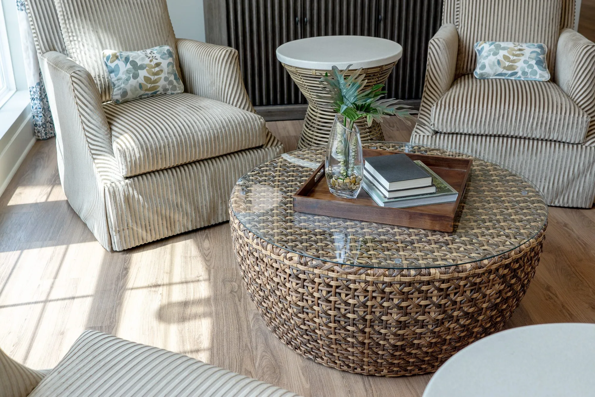 Senior living sitting room from above, a glass-topped woven drum table between two striped armchairs in sunlight