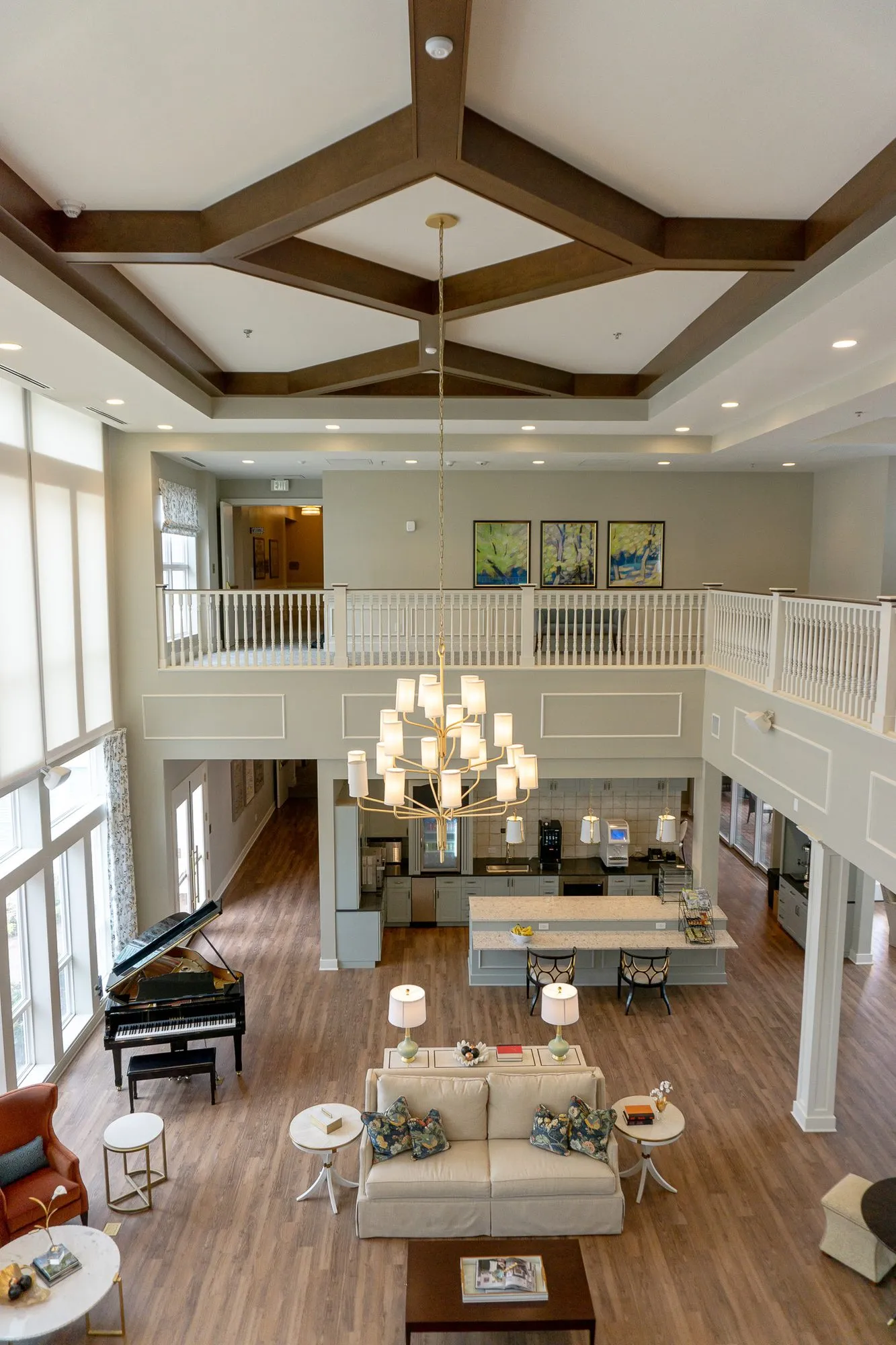 Senior living great room from above, a cream sofa, grand piano and kitchen island under a tiered chandelier