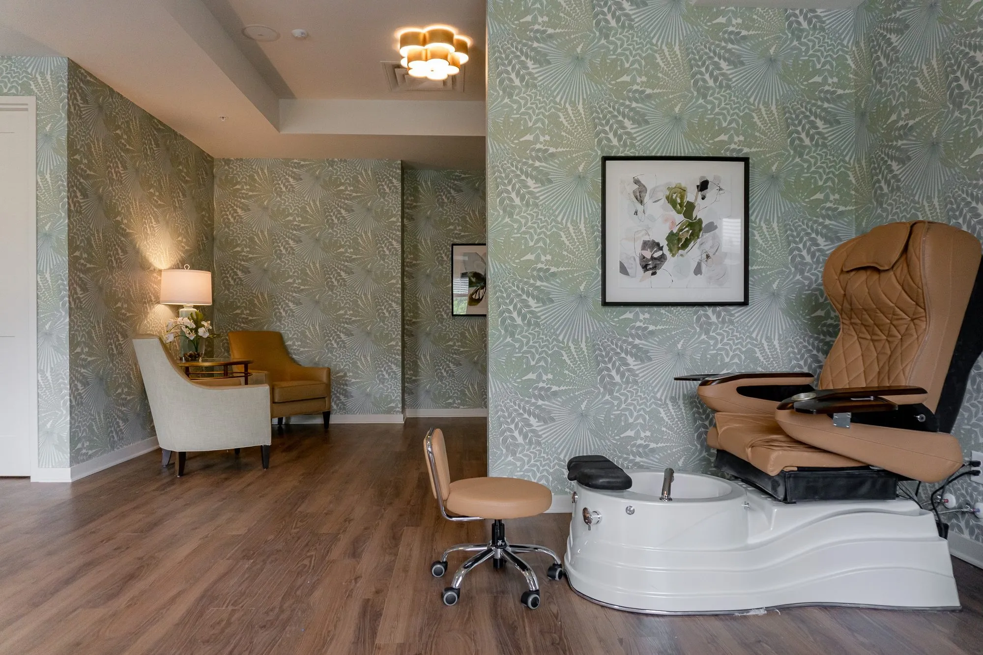 Senior living salon pedicure station with a rolling stool and white basin below a botanical print on palm frond wallpaper